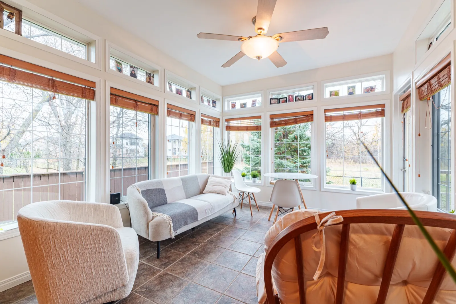 Four-season room with tall windows on three sides, transoms above, and a sofa and table set on tile