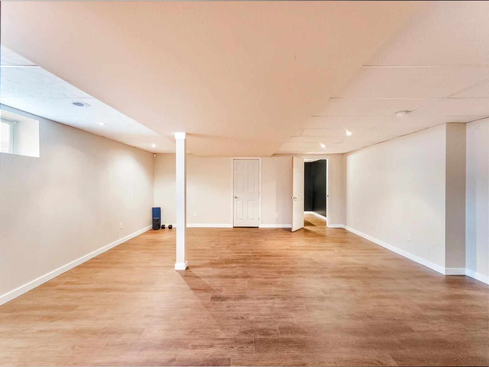 Finished basement rec room running the width of the house, white posts left open in the floor