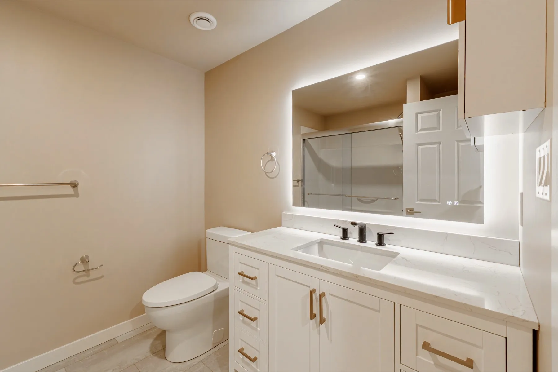 Basement bathroom with a white shaker vanity under a backlit mirror