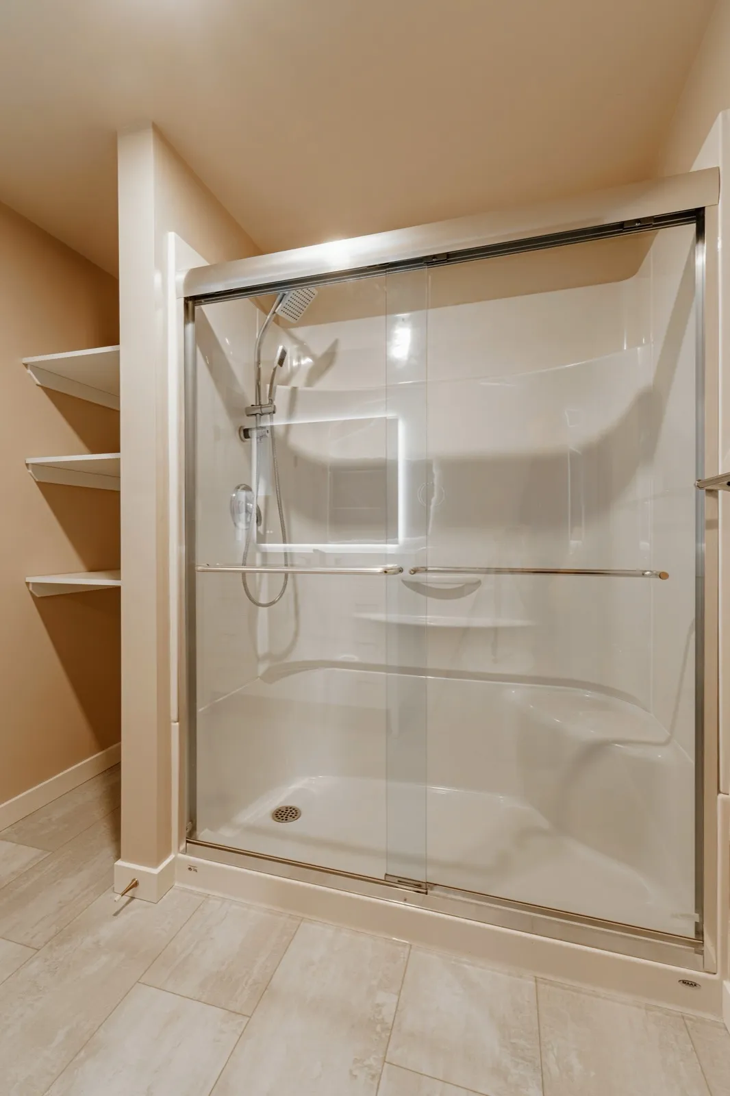 Walk-in shower behind a sliding glass door, open shelving alongside