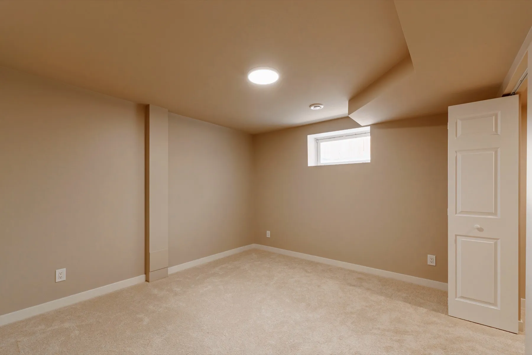 The bedroom from the doorway, carpeted and lit by a high window