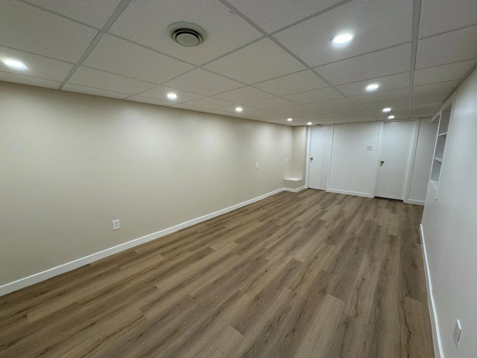 Finished basement running the width of the house, oak-look plank under a pot-lit tile ceiling