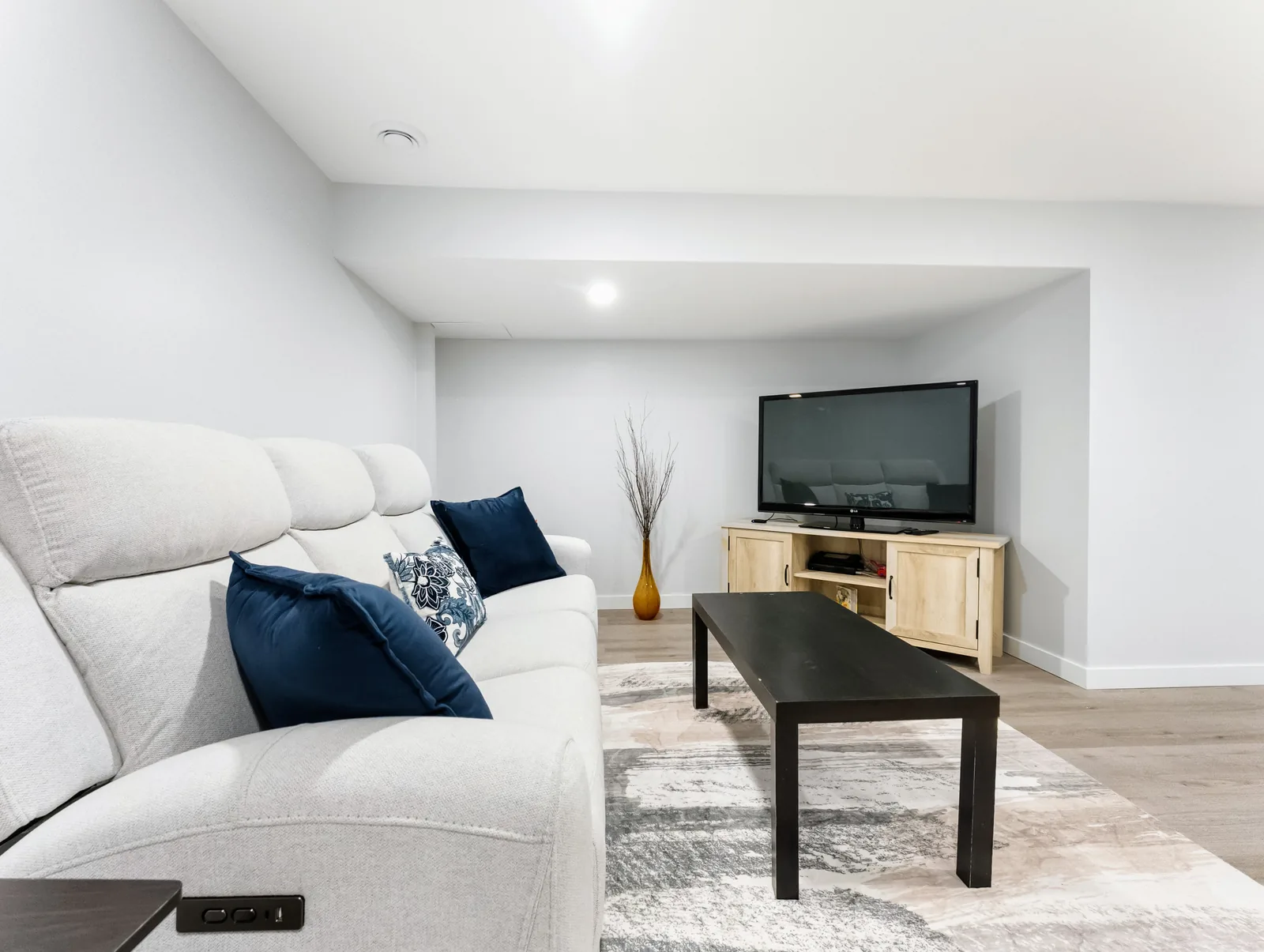 Finished basement living zone — pale sectional, low table and a TV on a light wood console