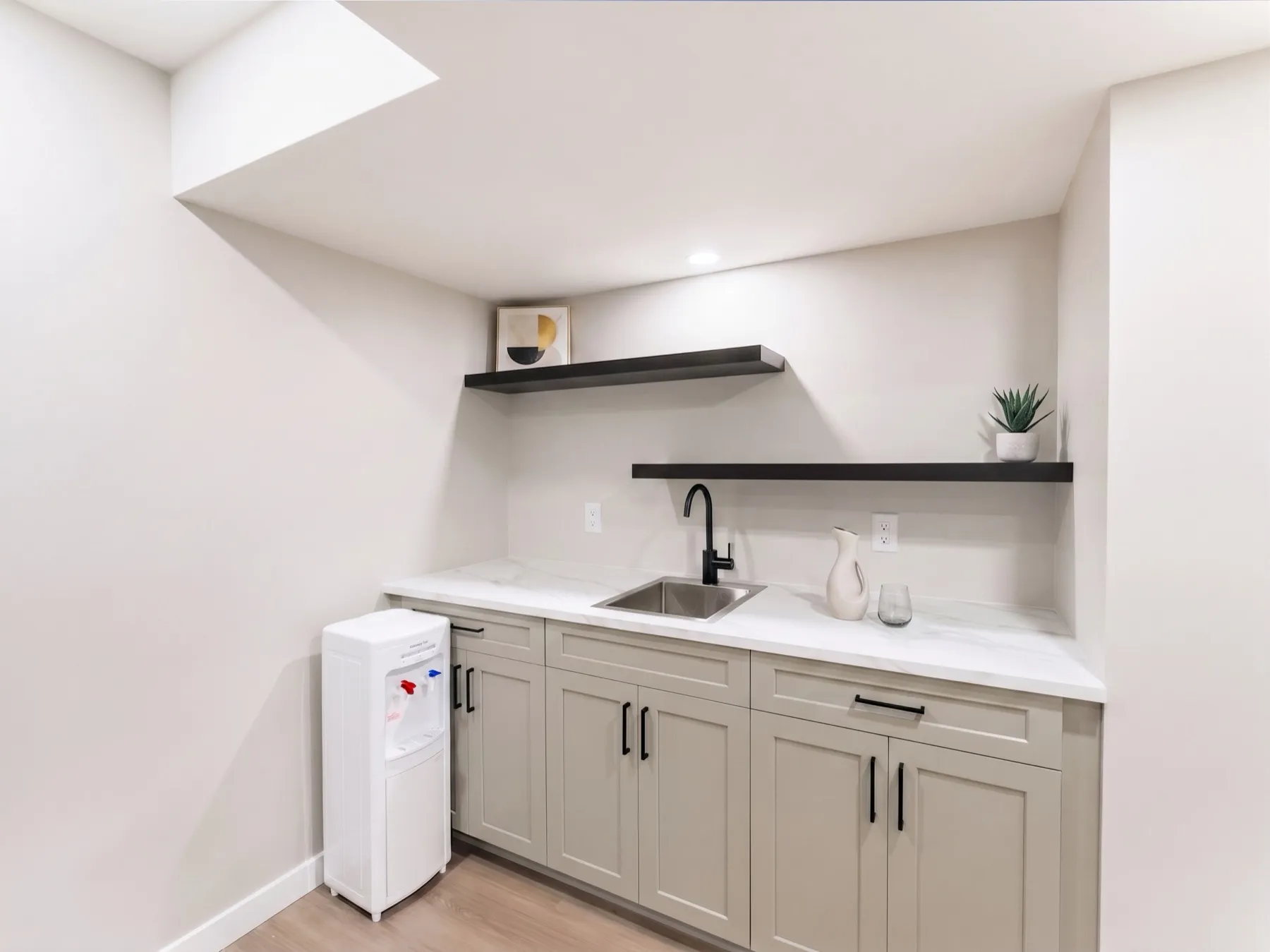 Basement kitchenette with sage-green shaker cabinetry, a marble-look counter and black floating shelves