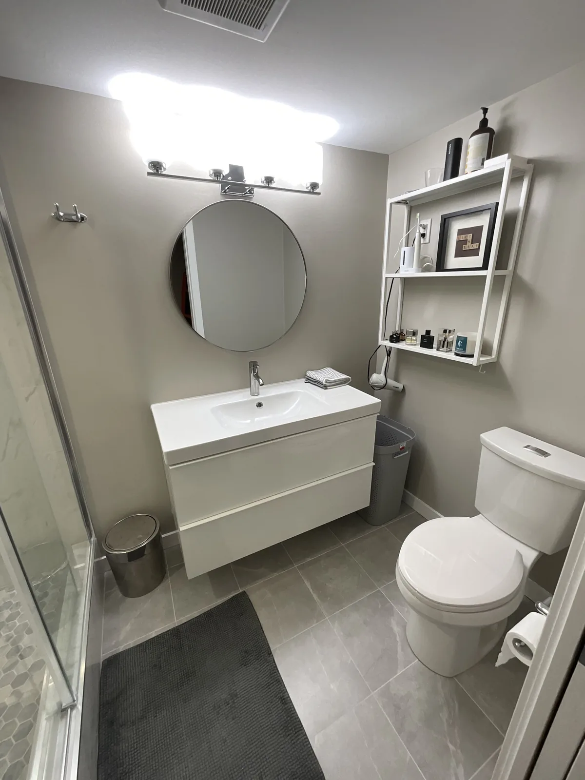 Bathroom with a wall-hung white vanity, round mirror and a large-format grey tile floor