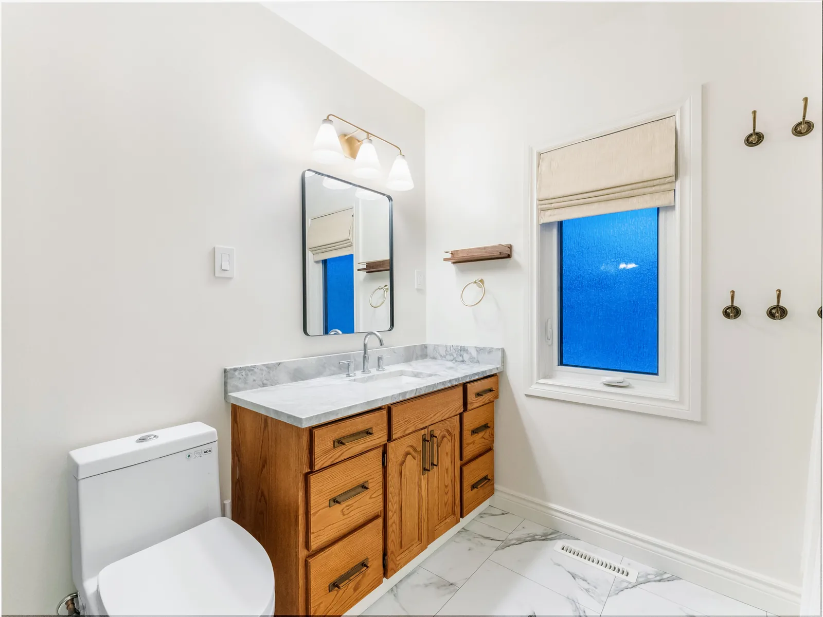 Bathroom with an oak vanity under a marble-veined quartz top, tub-shower along the far wall