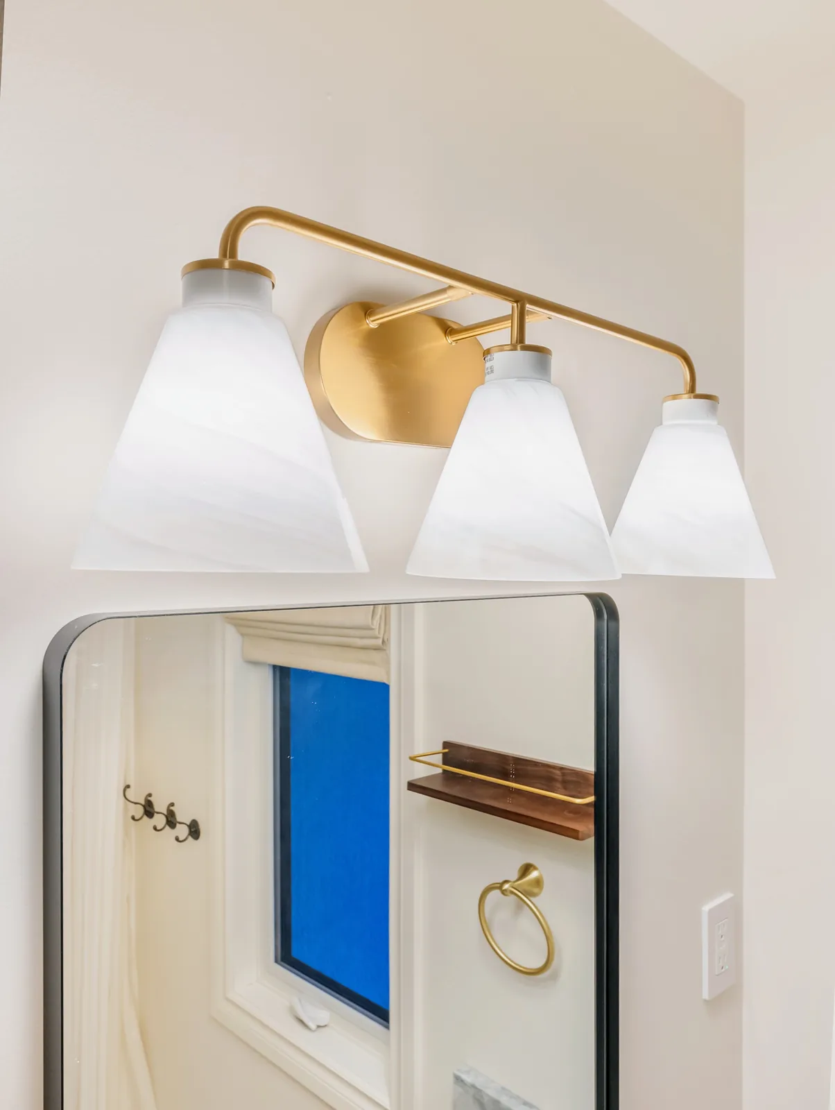 Brass three-light fixture above the mirror, towel ring and shelf to the side