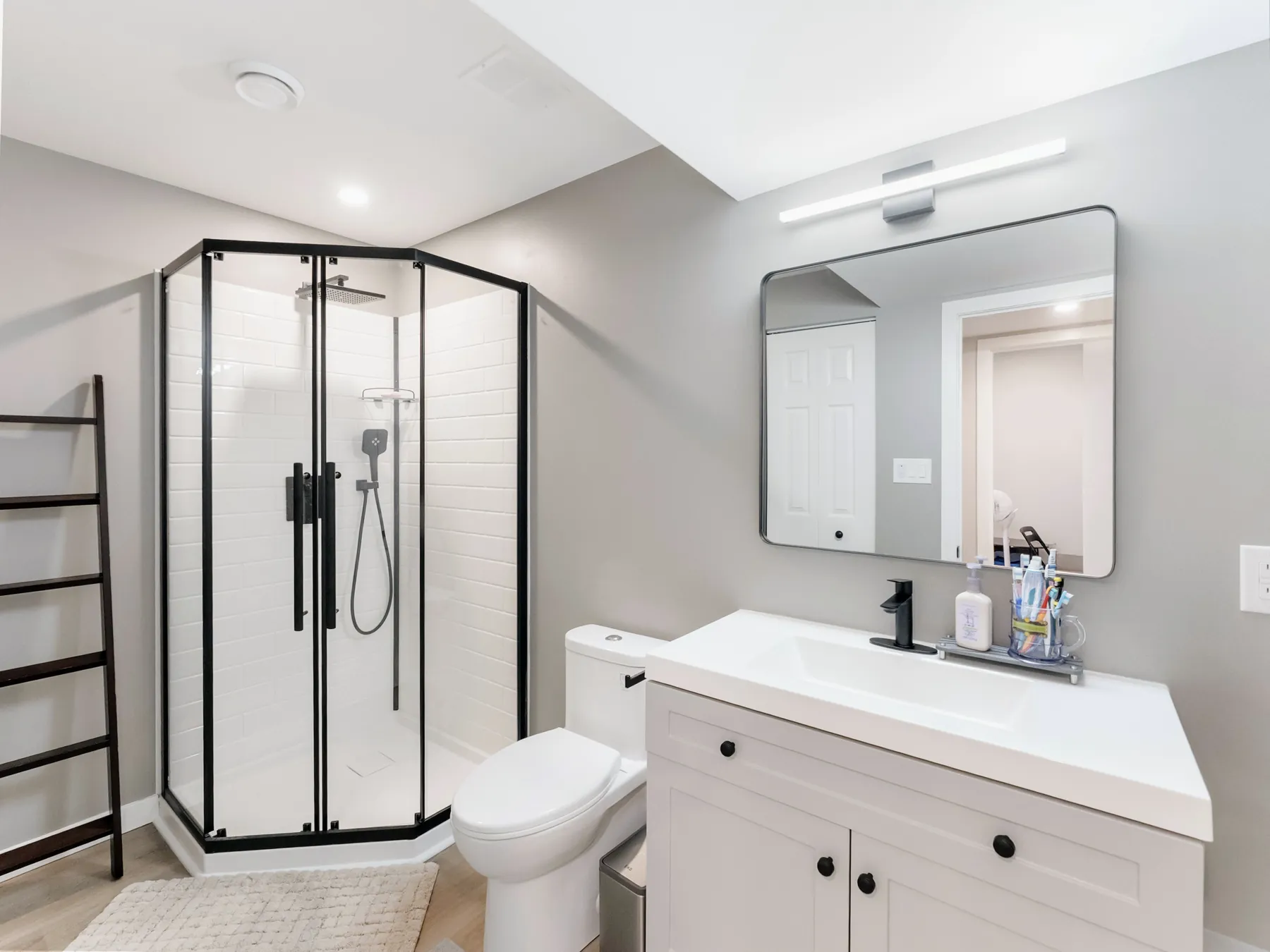 Three-piece bathroom with a black-framed neo-angle shower and white vanity