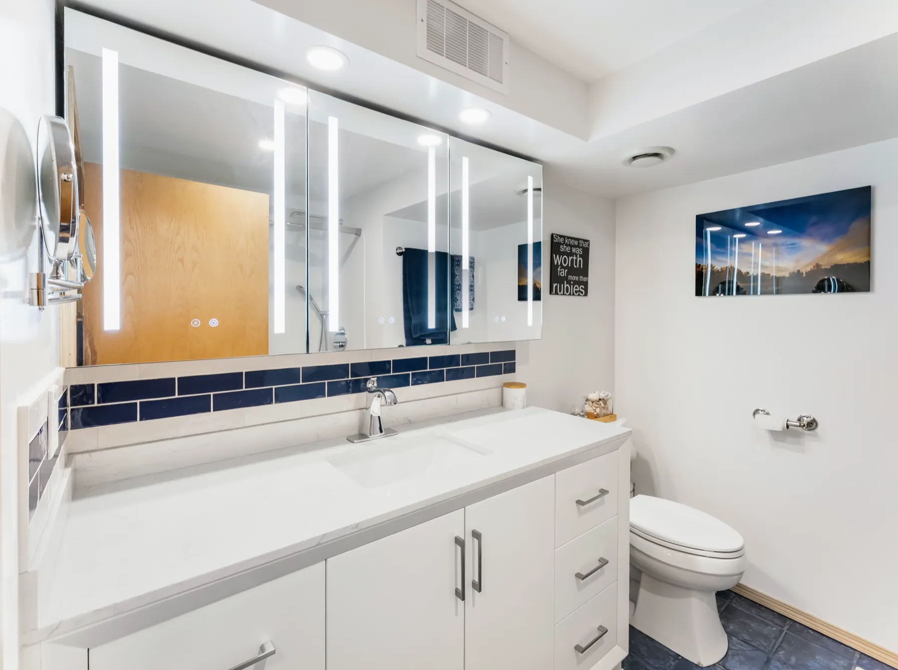 White bathroom with a long quartz vanity, a backlit mirror cabinet and a band of cobalt tile