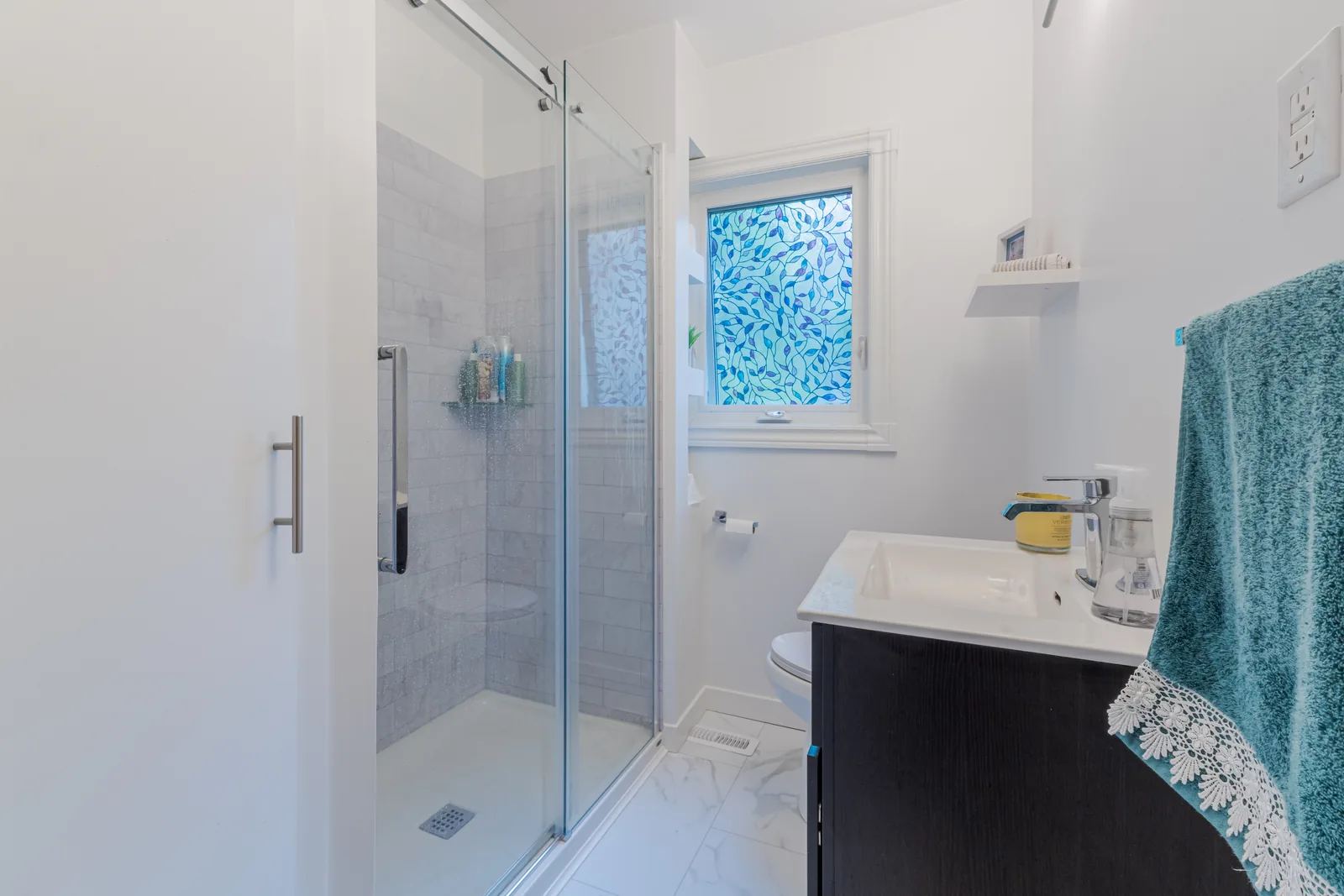 White bathroom with a sliding glass shower, dark espresso vanity and a marble-look porcelain floor