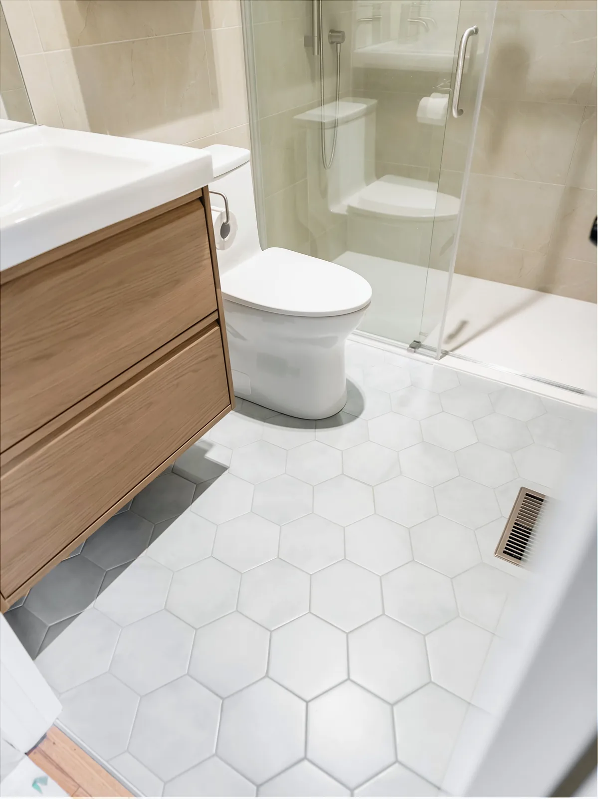 White hex floor tile against the wood-front vanity, looking through to the shower