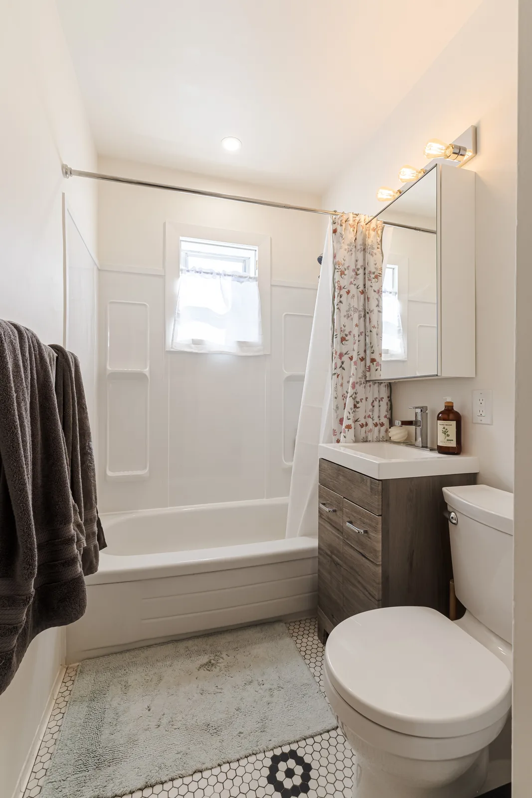 Bathroom with a white tub-shower, dark wood vanity and hex tile floor