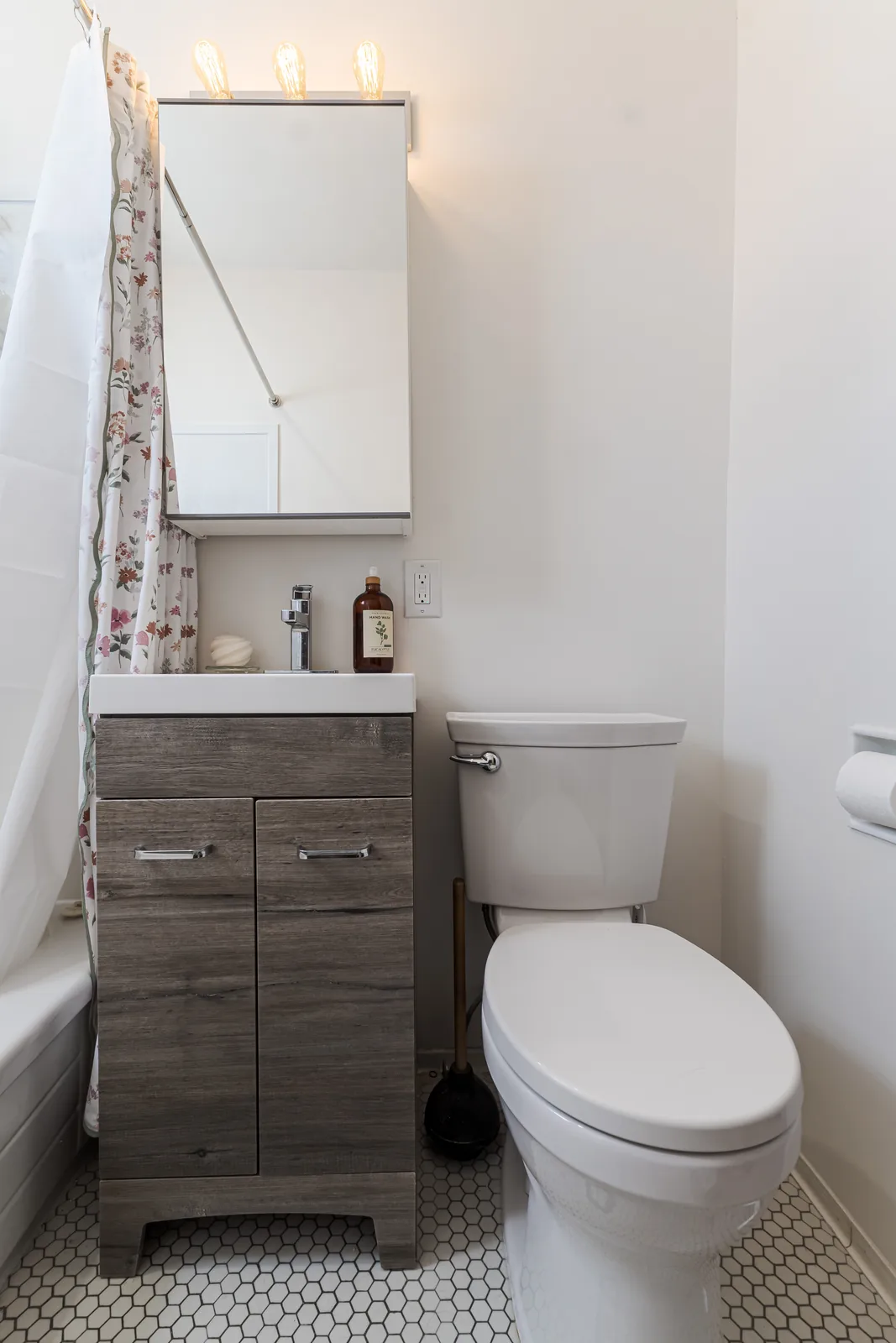 Wood vanity and mirrored cabinet, toilet alongside on hex tile