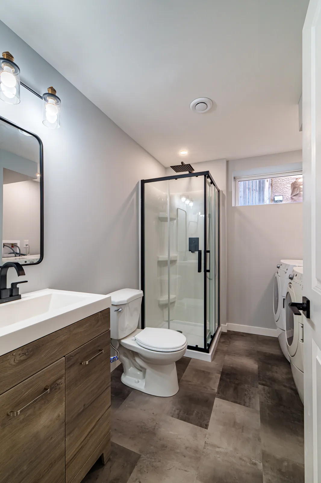 Basement bathroom with a dark wood vanity, arched mirror and a black-framed glass shower