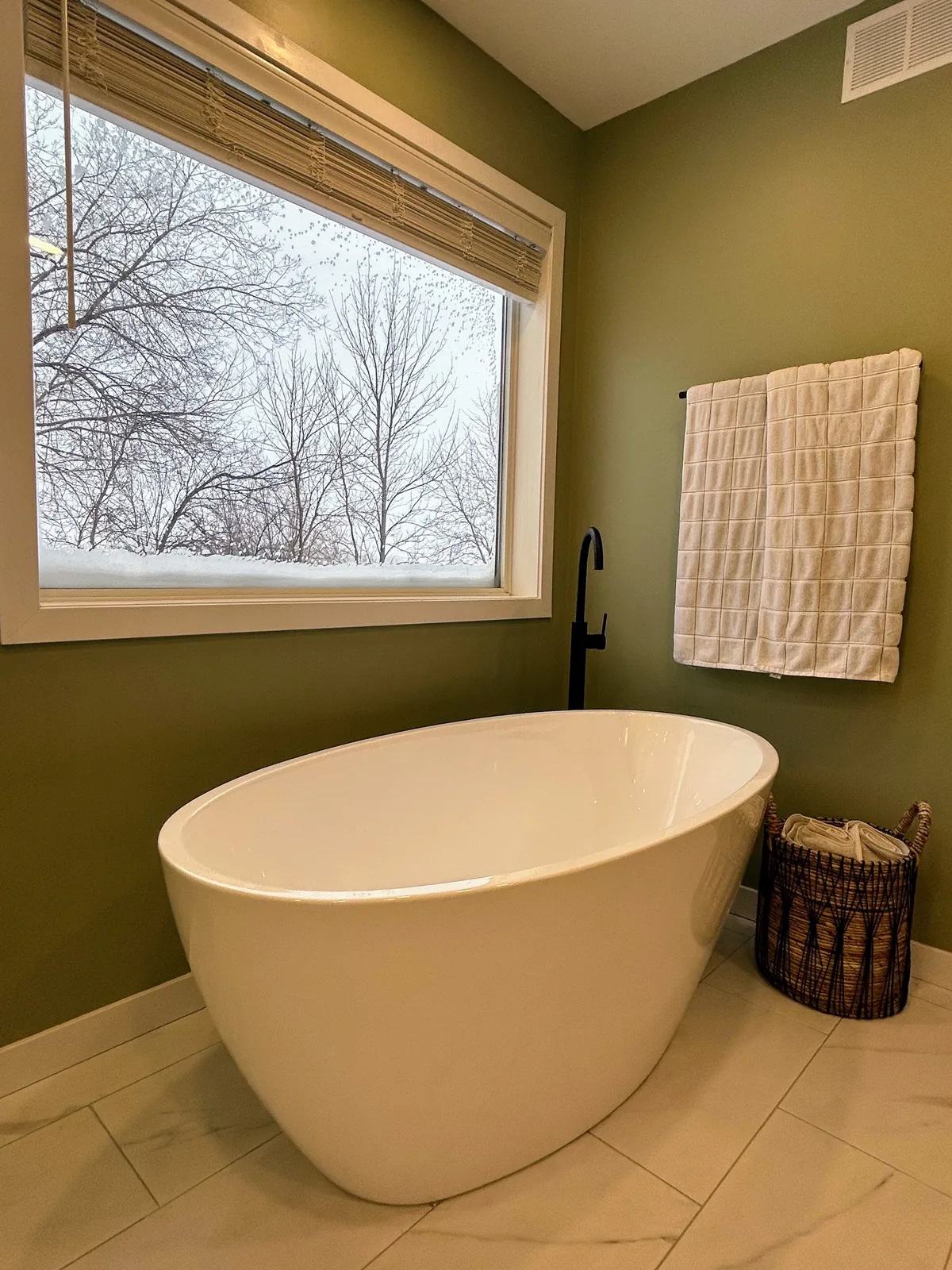 The tub from the foot, bare trees through the window beyond