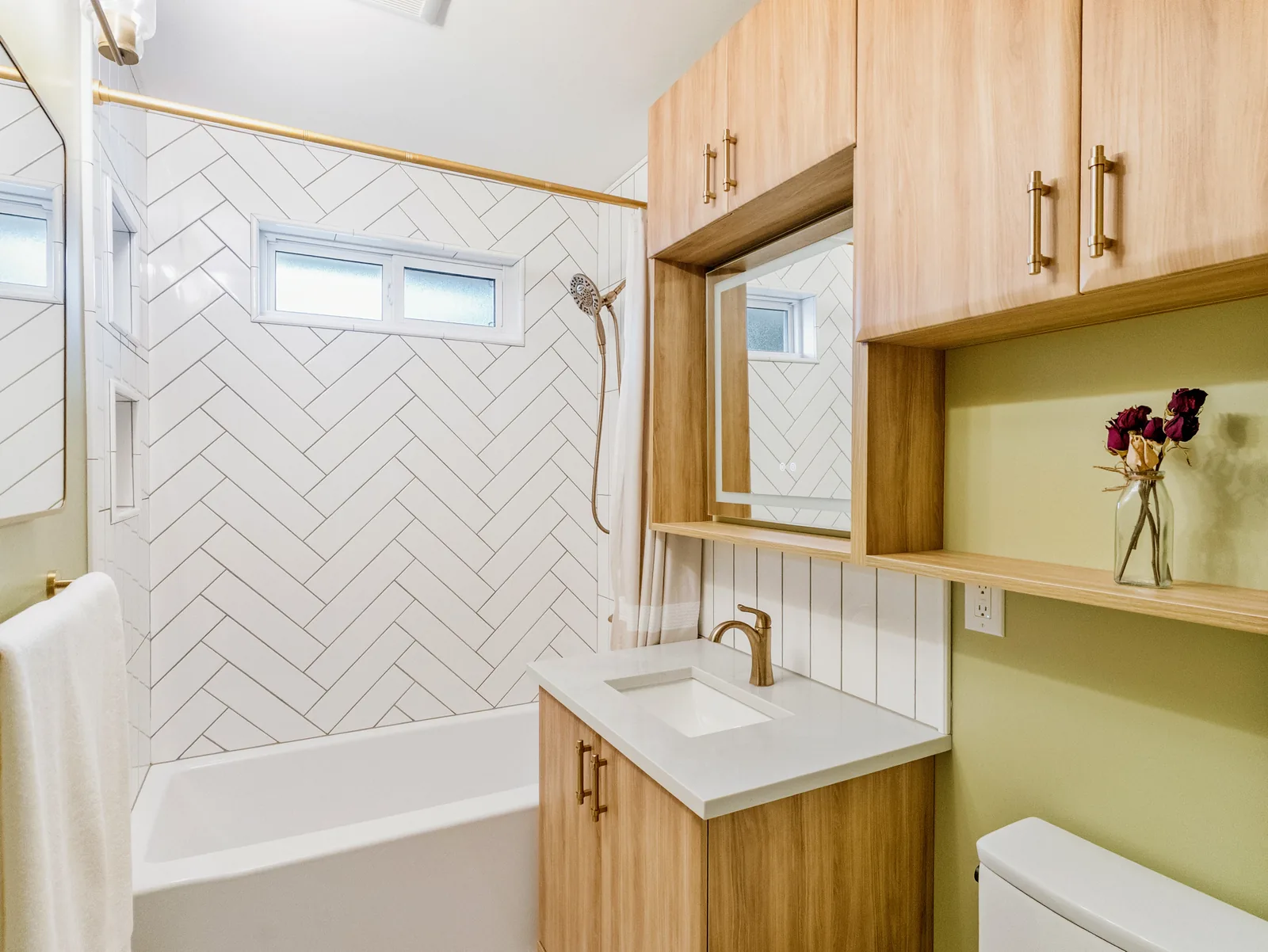 Oak wall cabinets over the toilet, mirror and shelf above the vanity