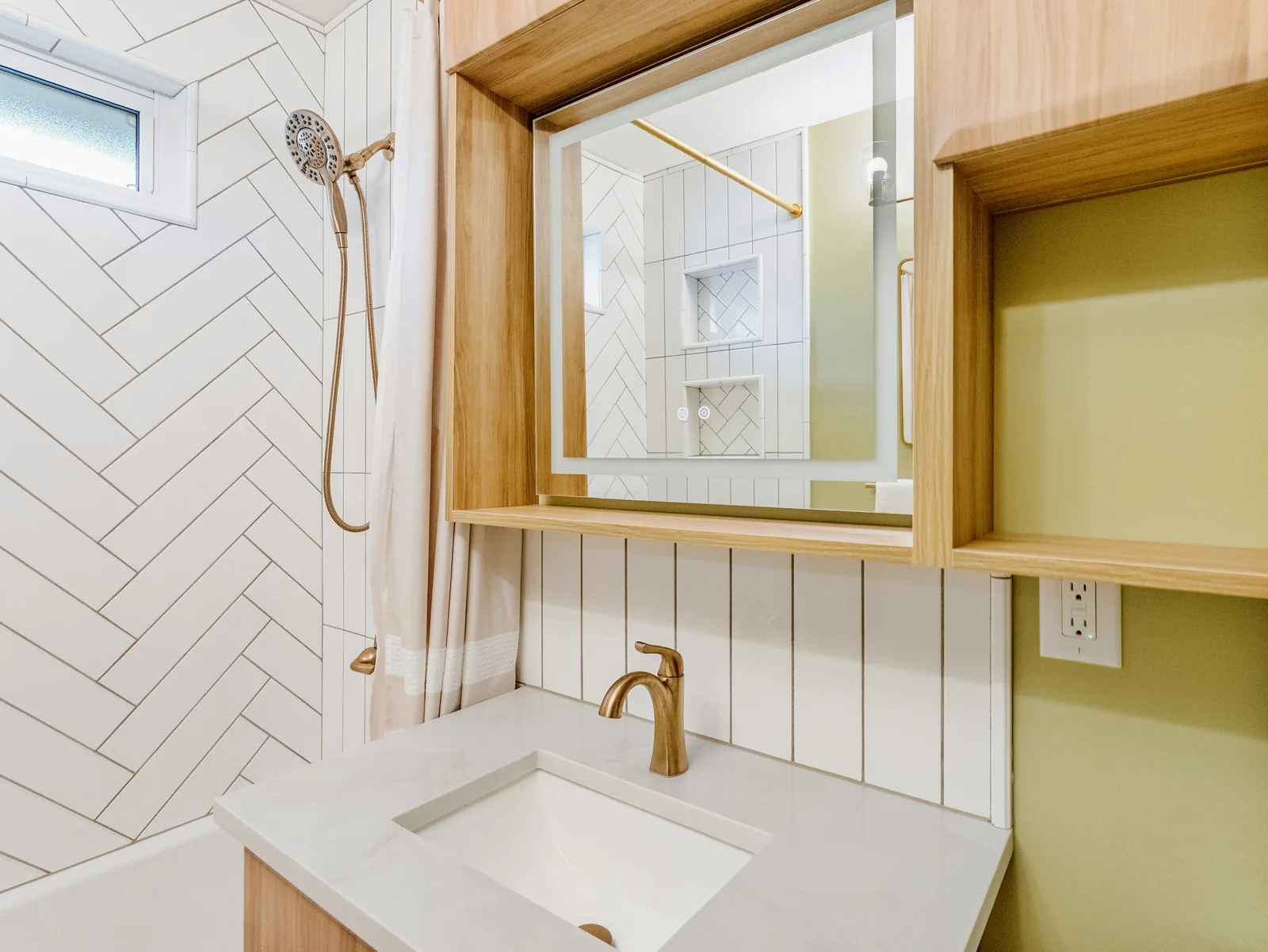 Oak-framed mirror over a white basin, brass tap against white herringbone tile