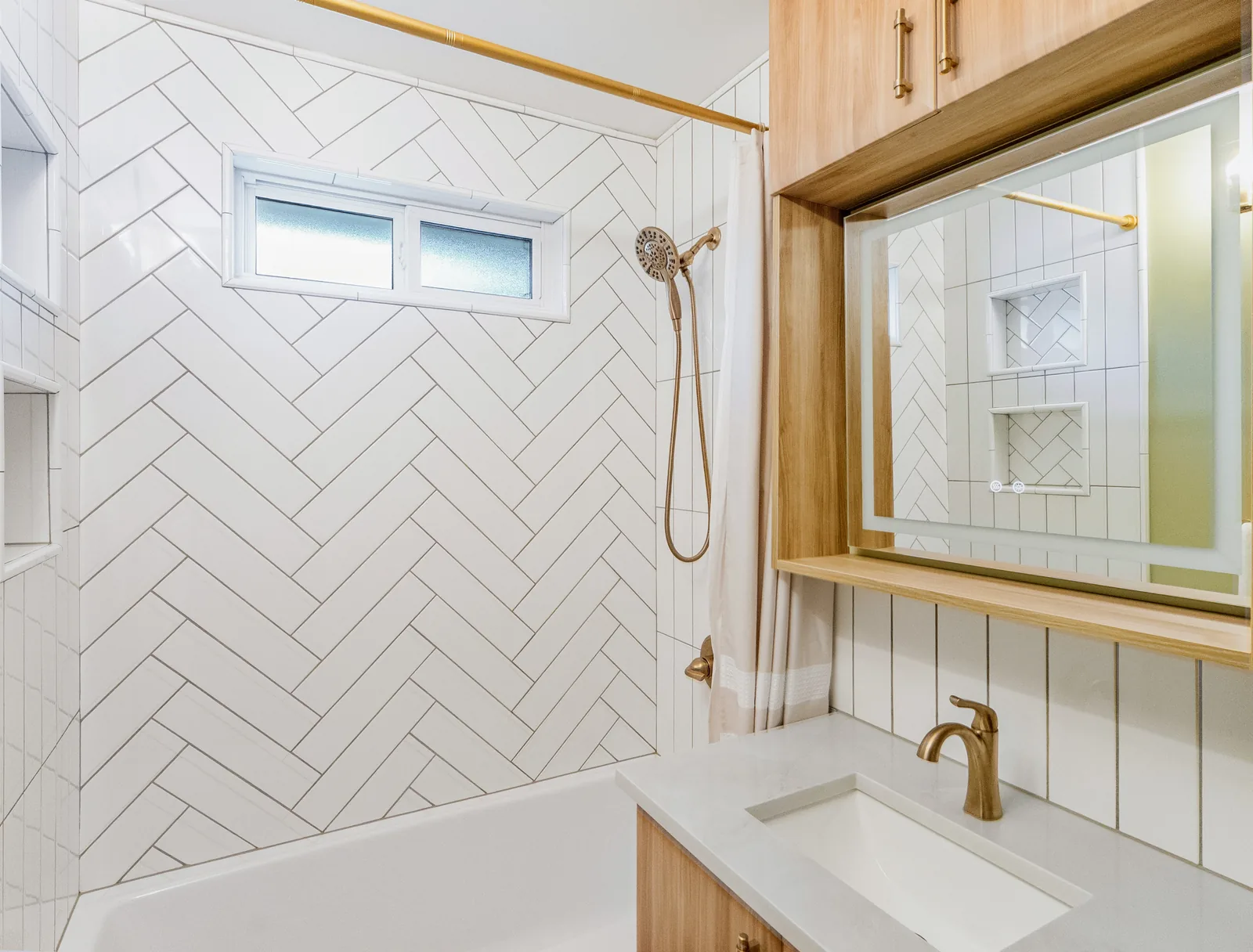 Brass hand shower on the herringbone wall, window set above the tub