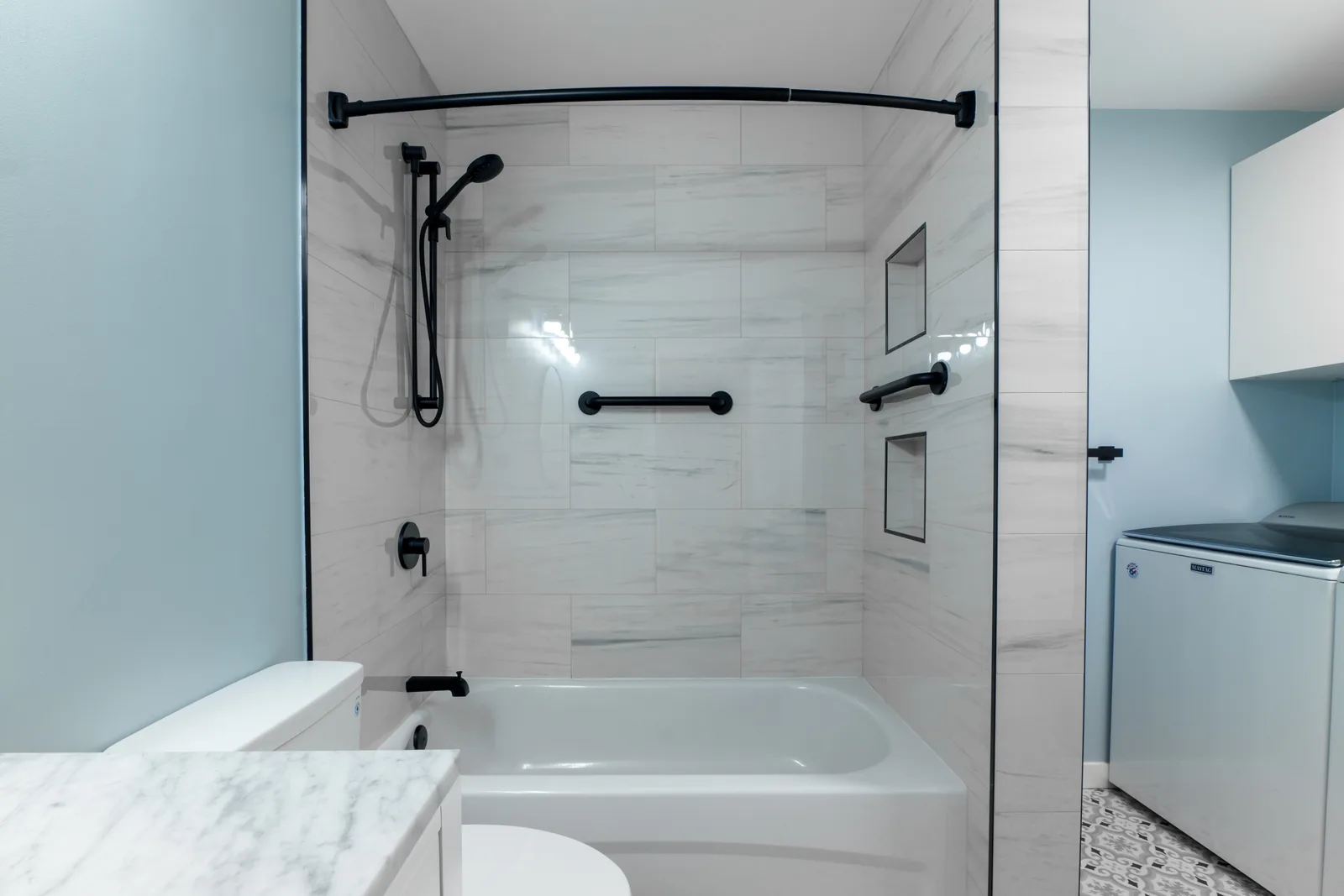 Tub-shower with a curved rail, niches set into the marble-look tile