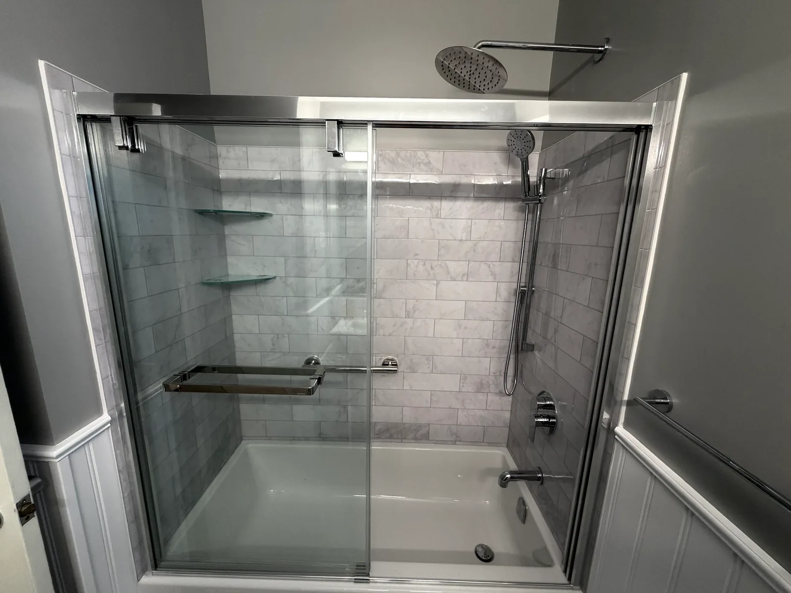 The tub and shower straight on, rain head and hand shower against the tile