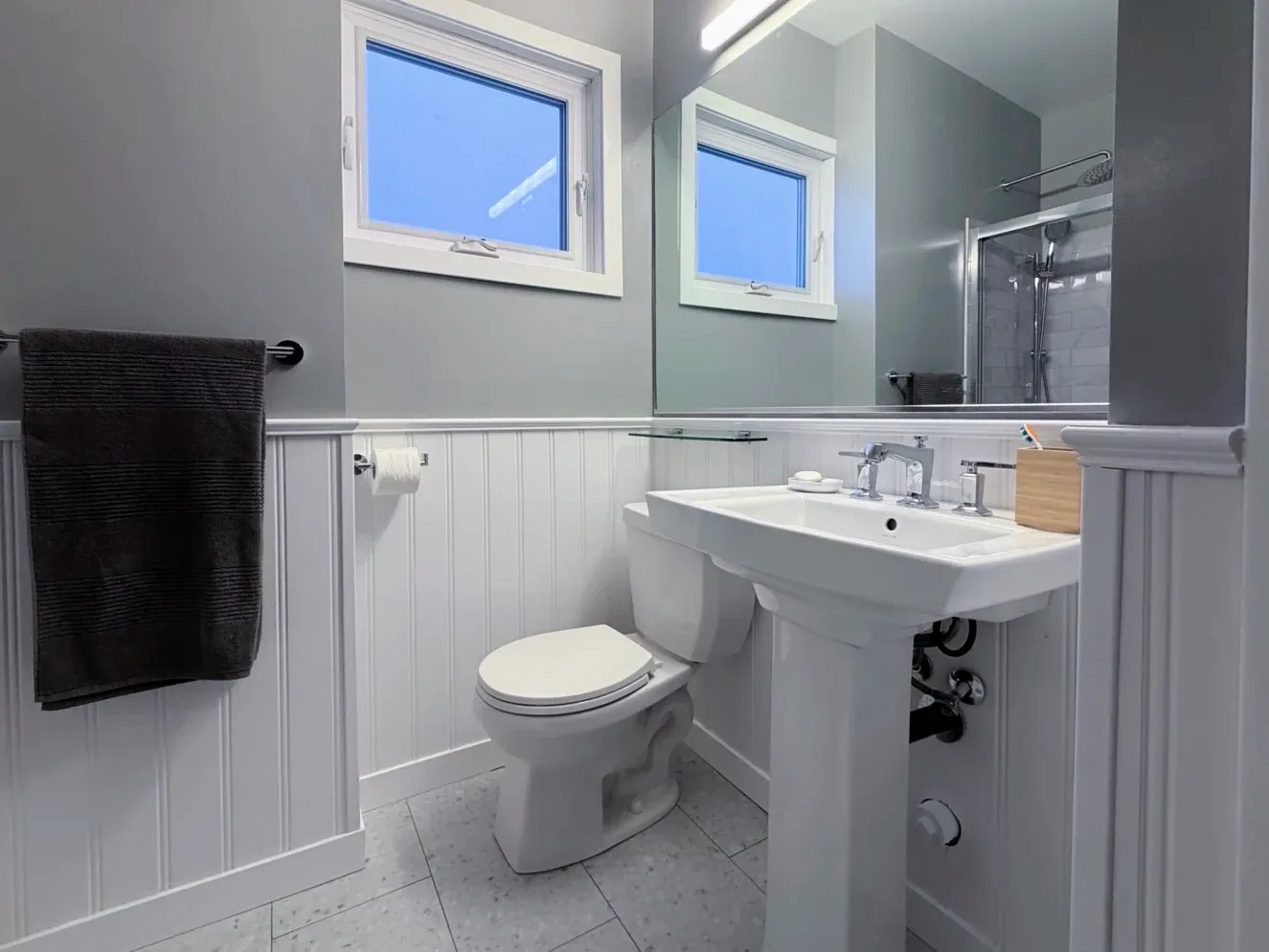 Pedestal sink and toilet under the two windows, beadboard running the wall