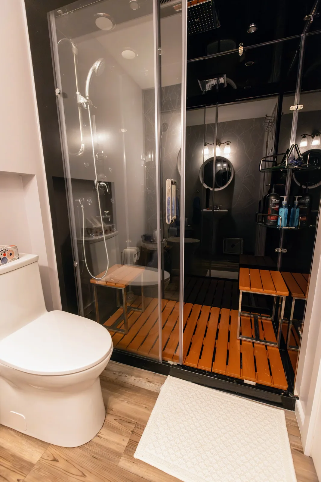 The cabin's sliding doors open on the teak bench, rain head above