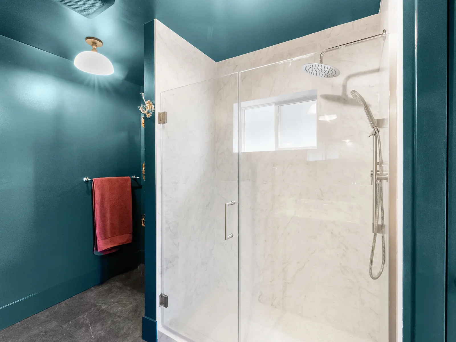 Frameless glass shower in marble-look tile, set against the teal wall