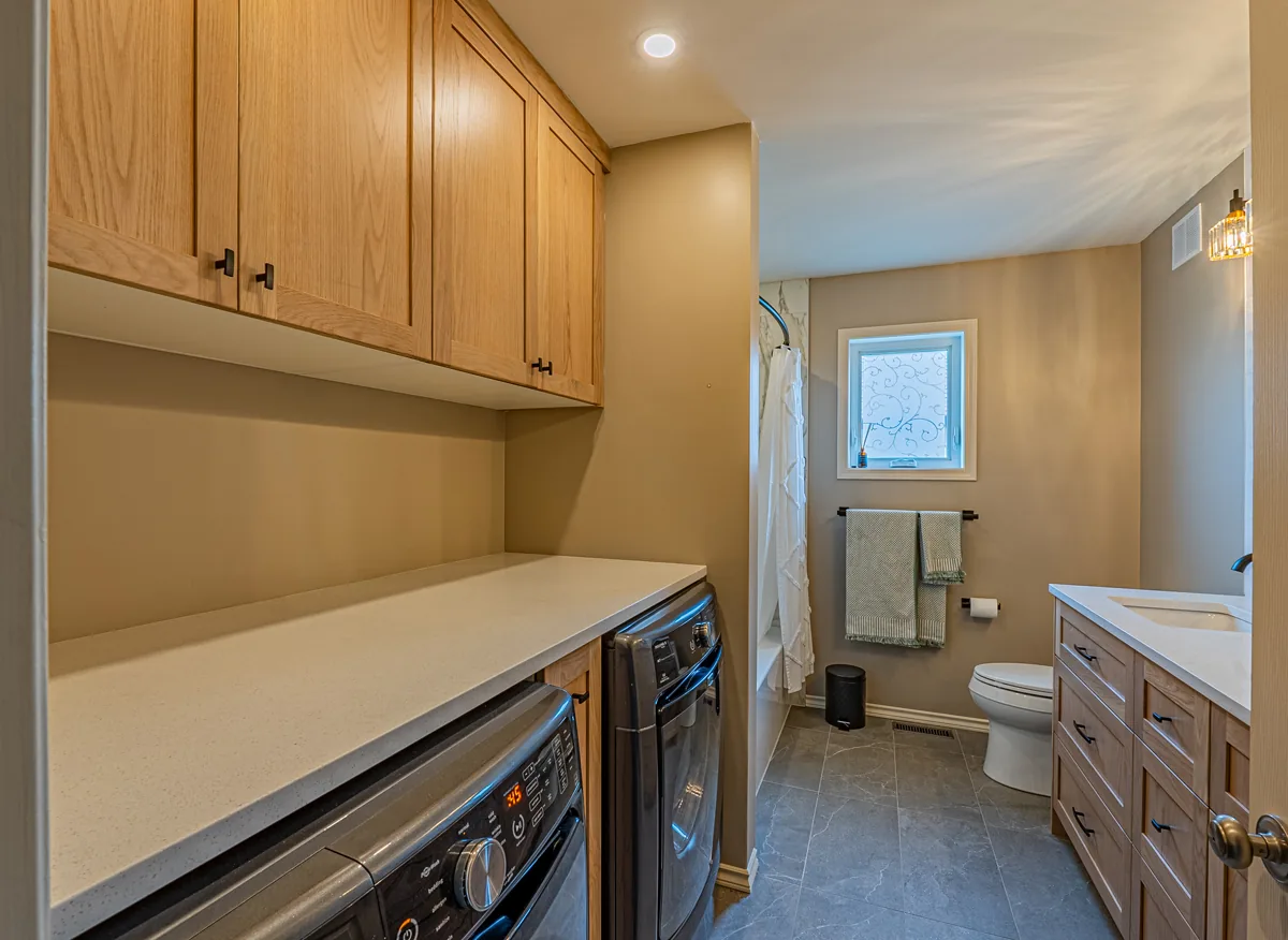 The main bathroom's laundry pair under a white counter and oak uppers, the vanity and window beyond