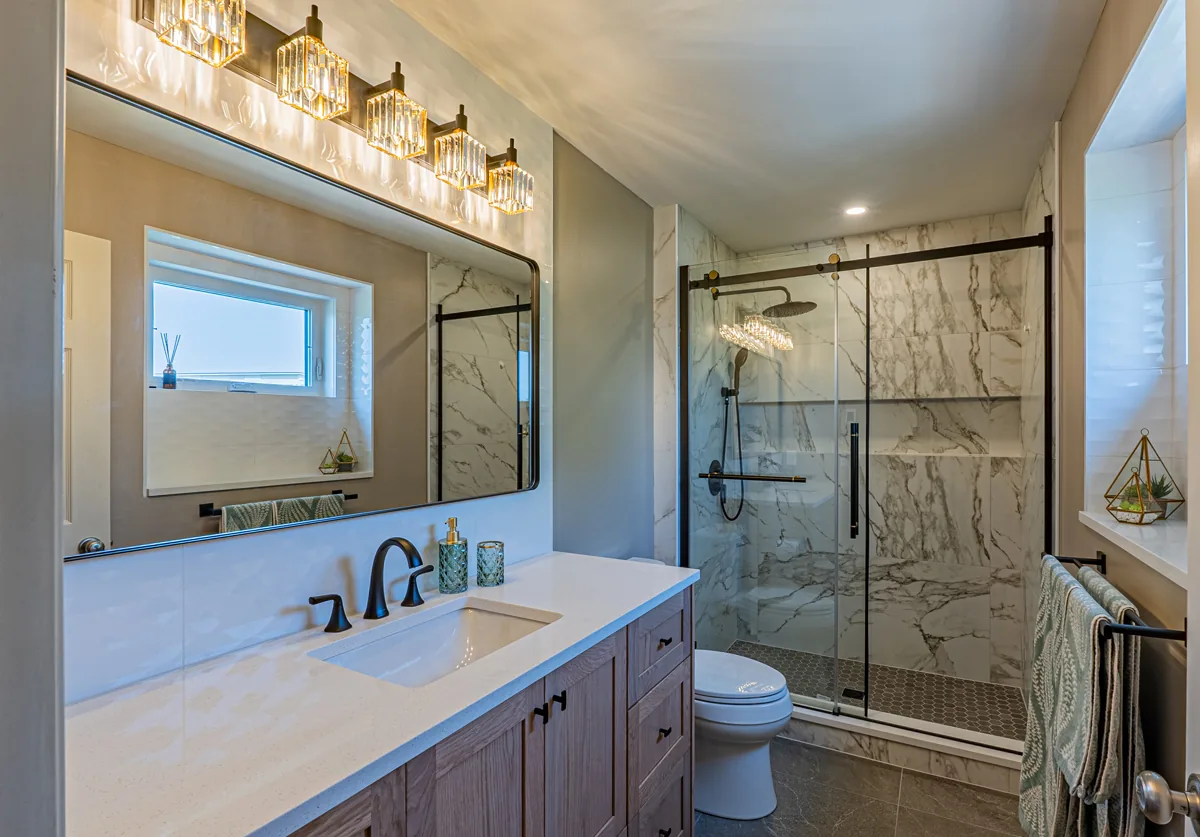 The ensuite vanity under one wide black-framed mirror, the walk-in shower beyond