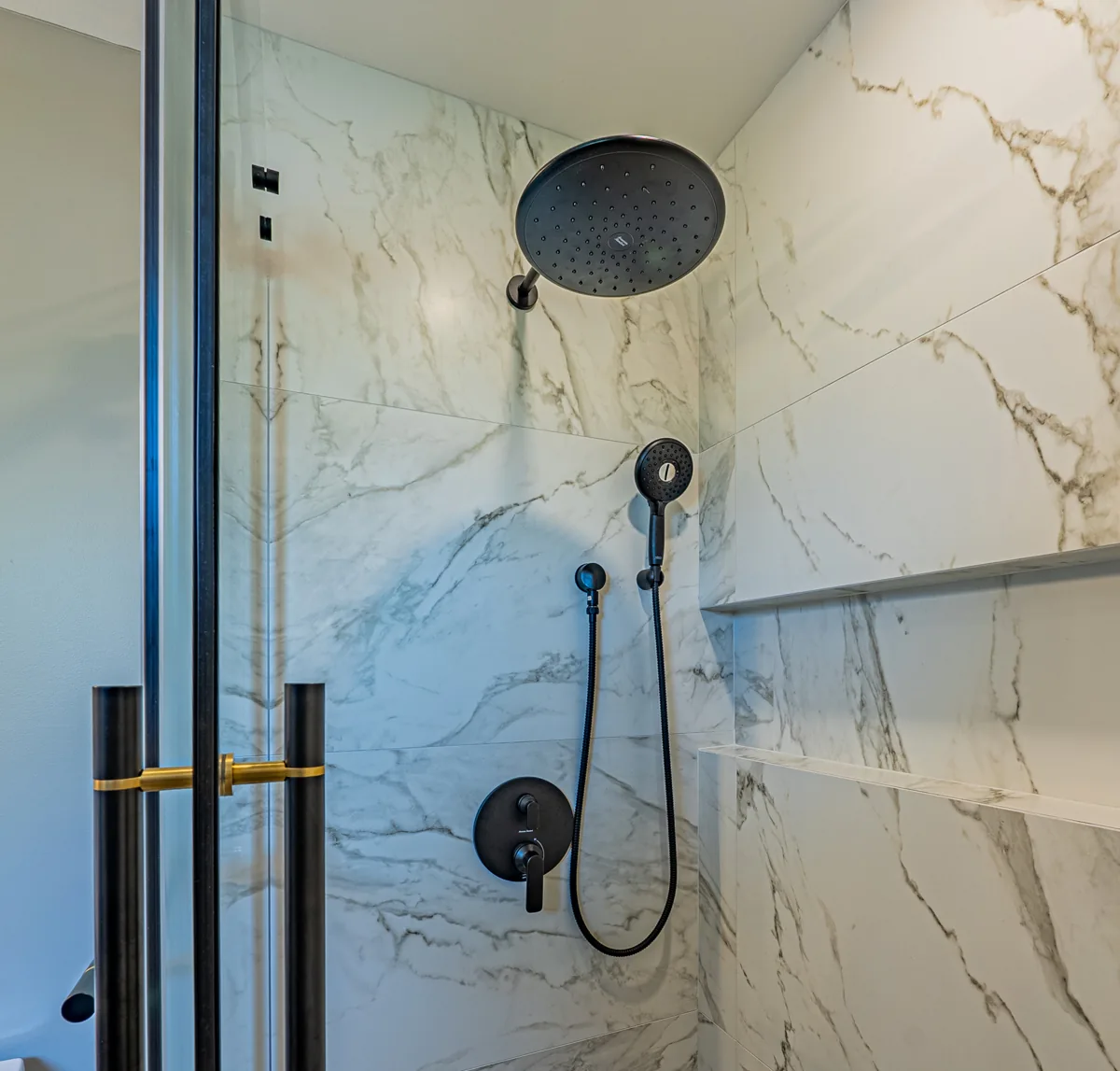 Inside the ensuite shower: marble-look slab tile with a black rain head and hand shower