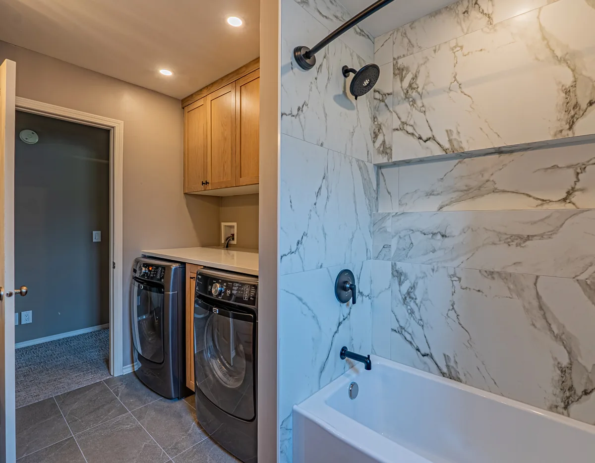 The main bathroom's tub-shower in marble-look tile, the laundry pair by the door