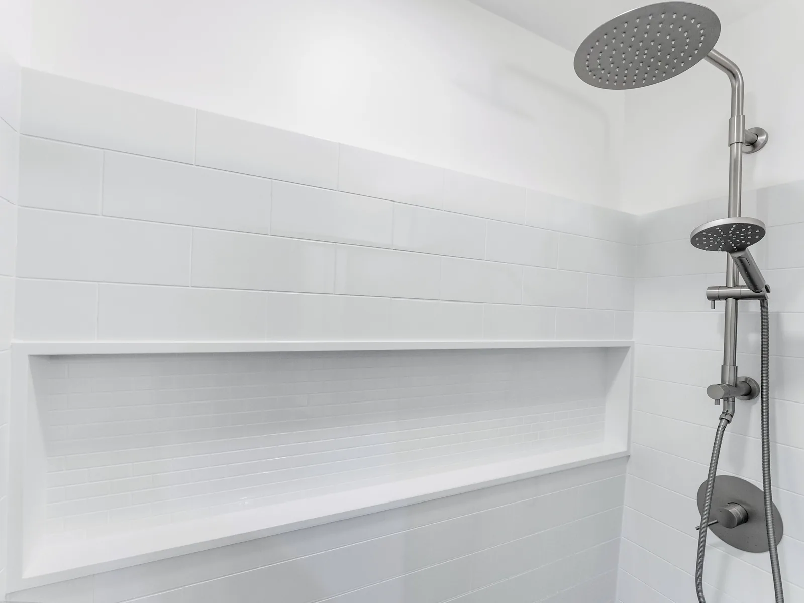 The shower surround in full, chrome fittings against white panelling