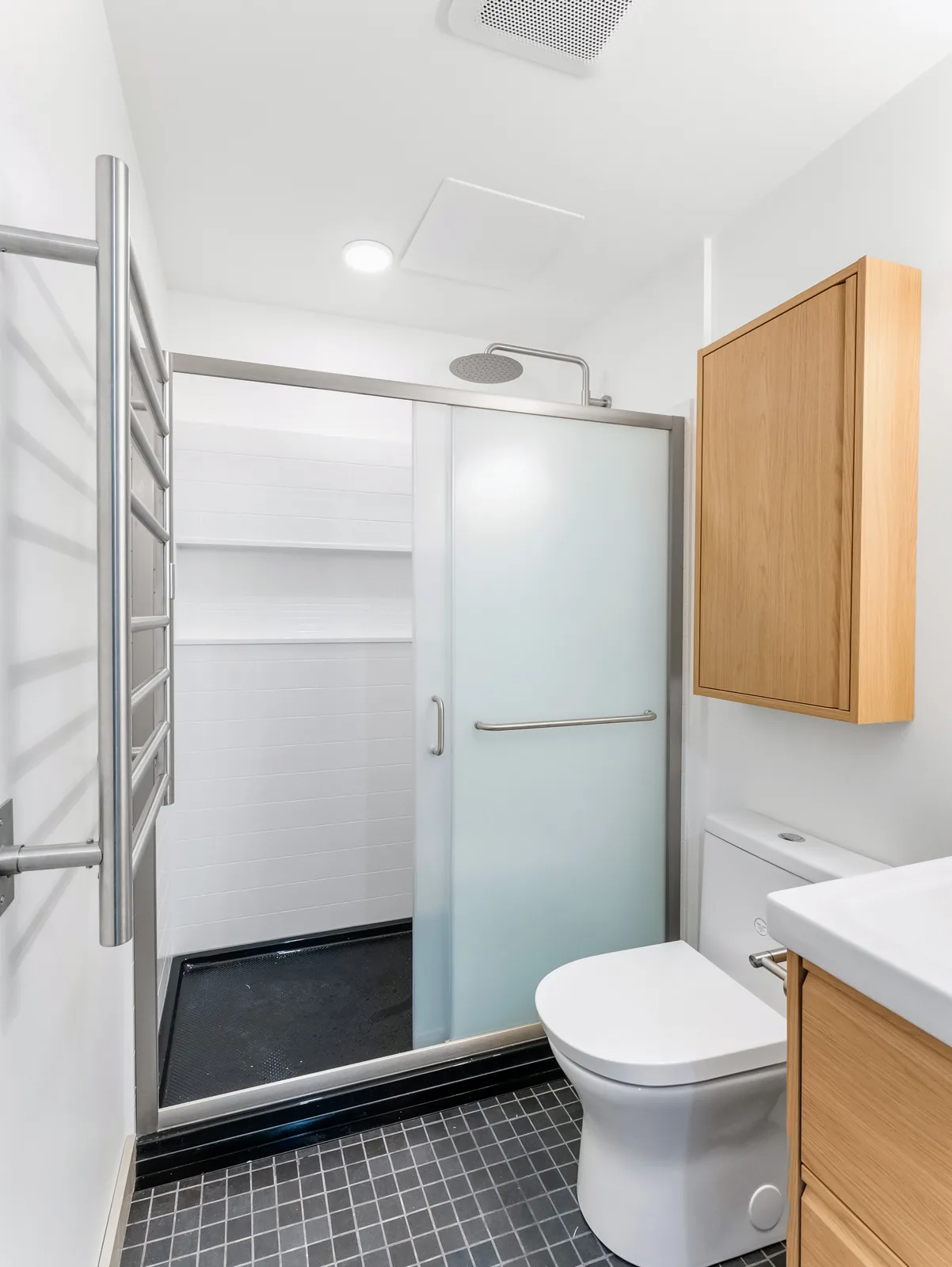 Heated towel ladder beside the frosted shower door, charcoal tile underfoot