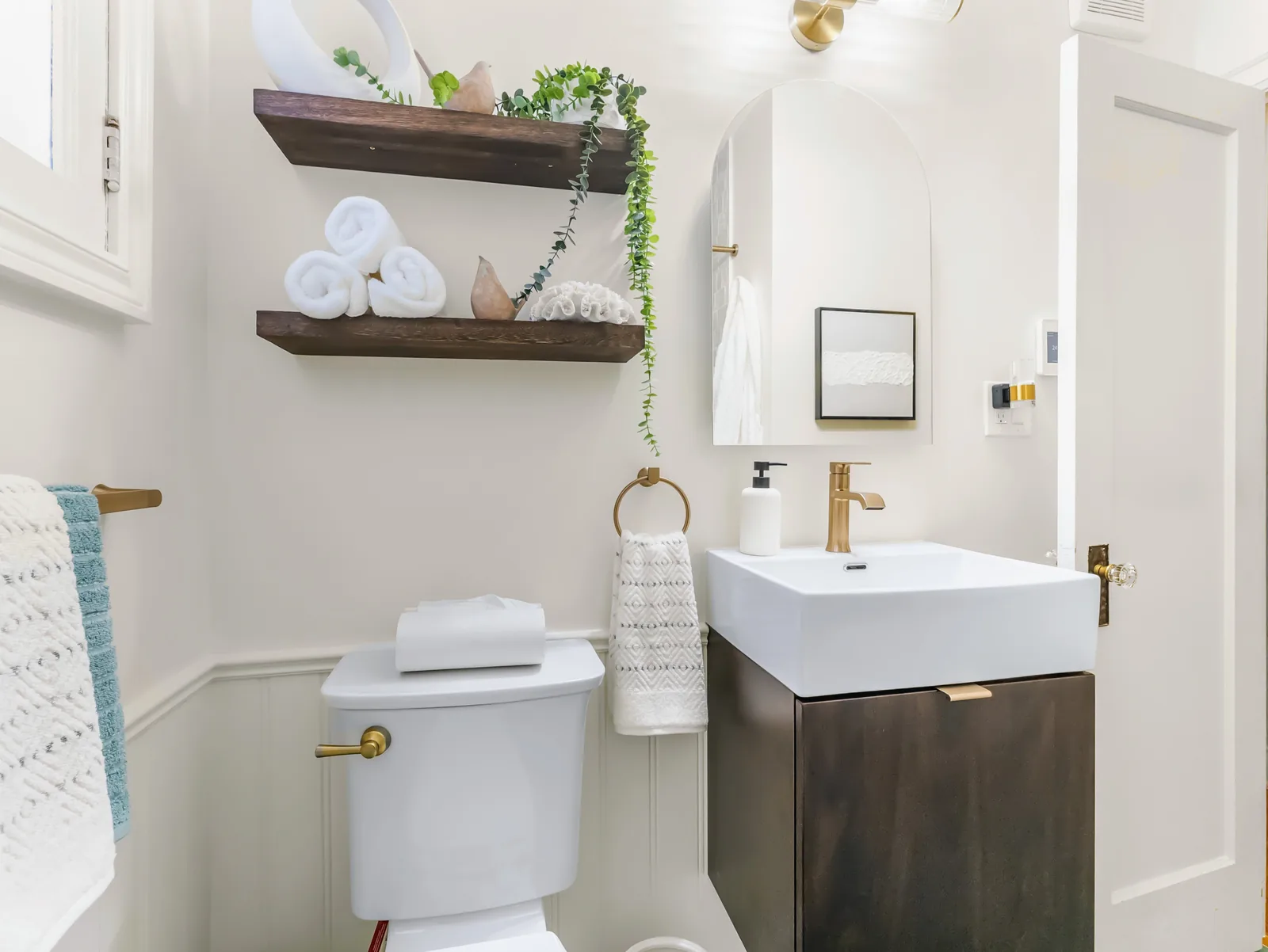 Dark floating shelves over the toilet, arched mirror and brass tap on the vanity