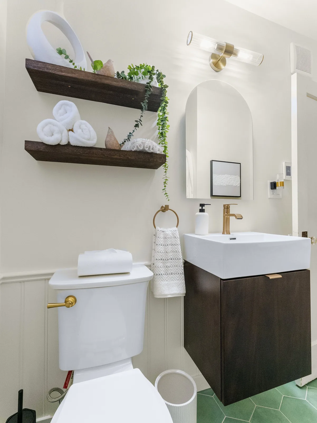 Arched mirror above the wall-hung vanity, brass fittings against white panelling