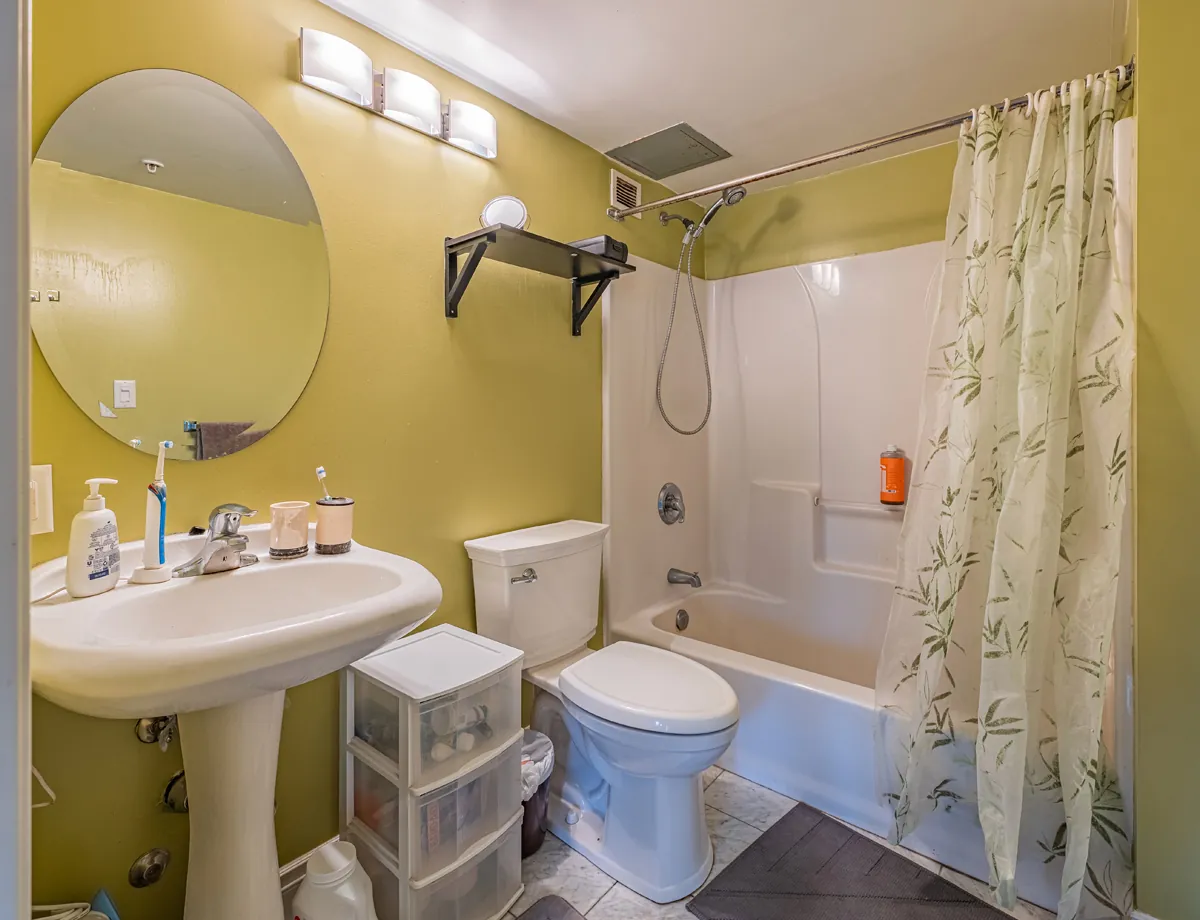 Before: the bathroom, a pedestal sink and a tub surround against green walls