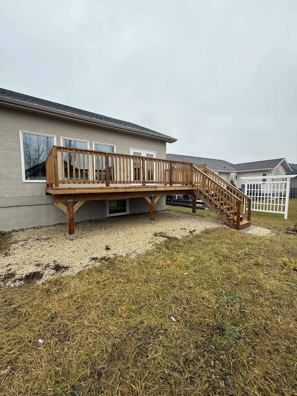 The cedar deck from the yard on a wet day, its stair running down to the gravel