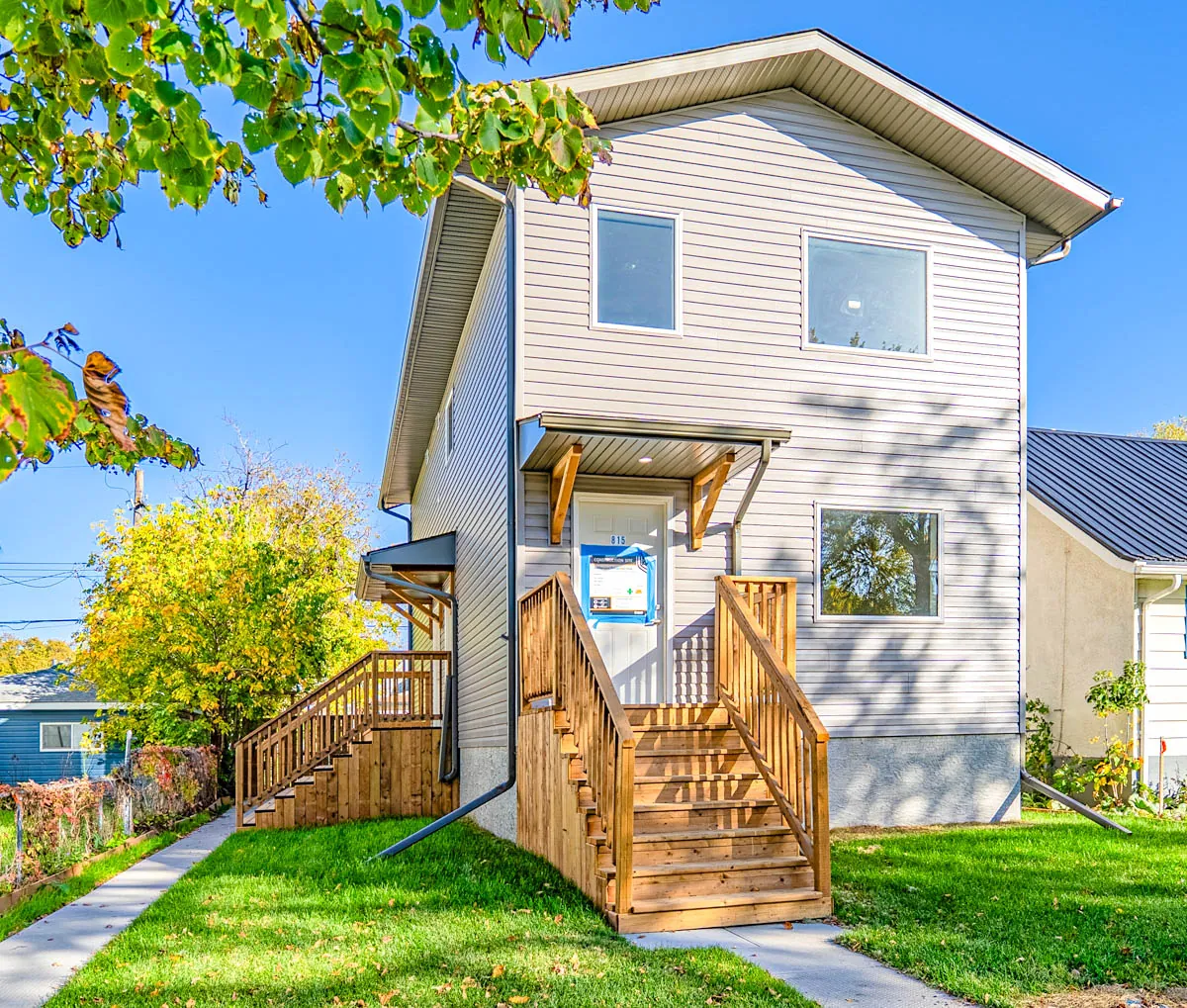 The finished infill from the front corner — new siding, cedar stairs and a city permit notice still on the door