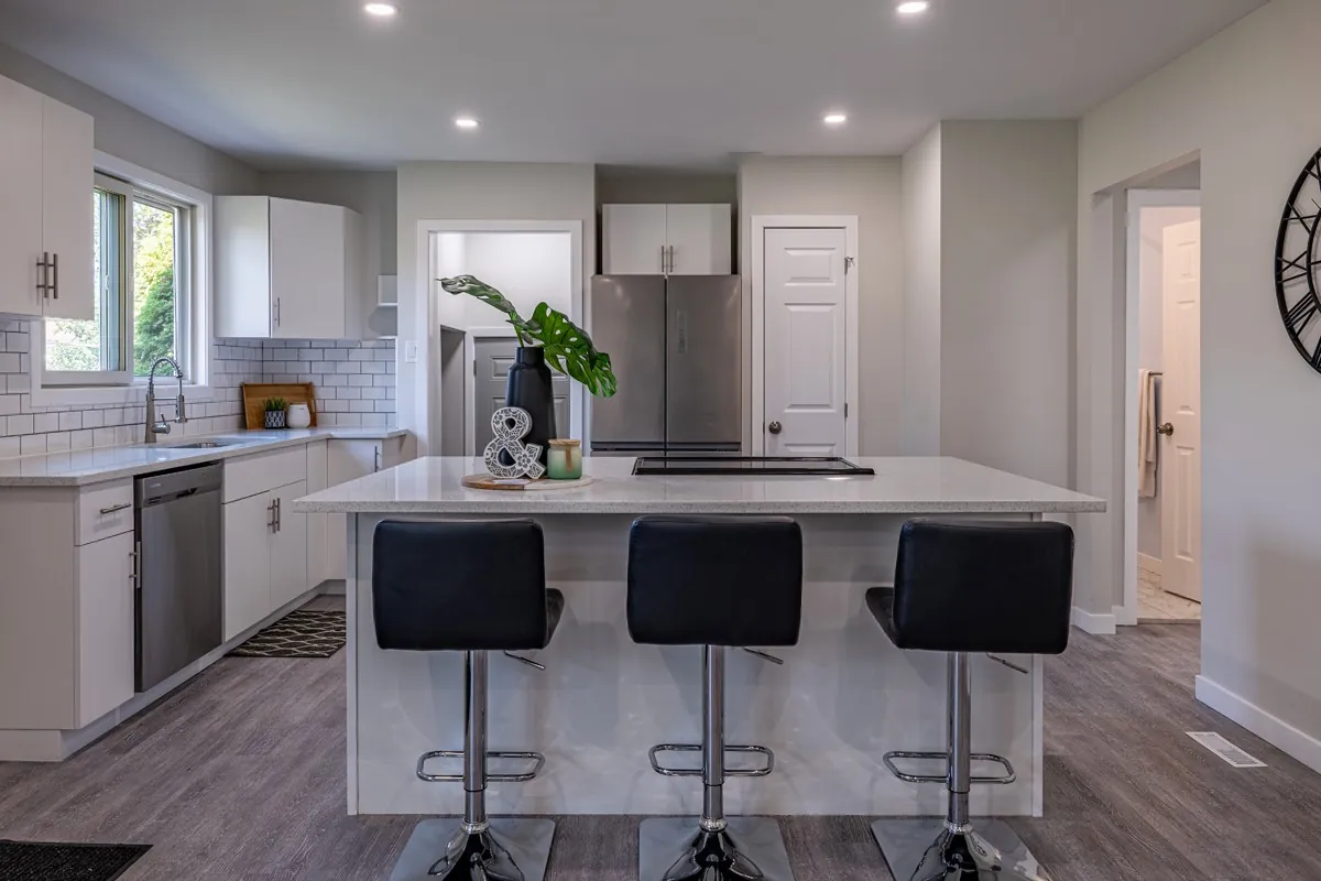 White kitchen with a long island and three black stools, open through to the hall