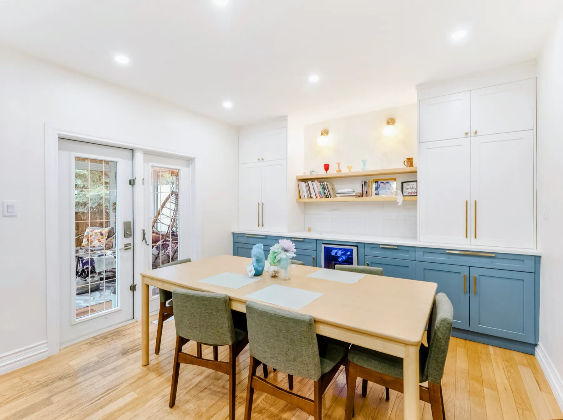 Slate-blue shaker cabinetry along a dining wall, with white uppers, brass handles and french doors beyond
