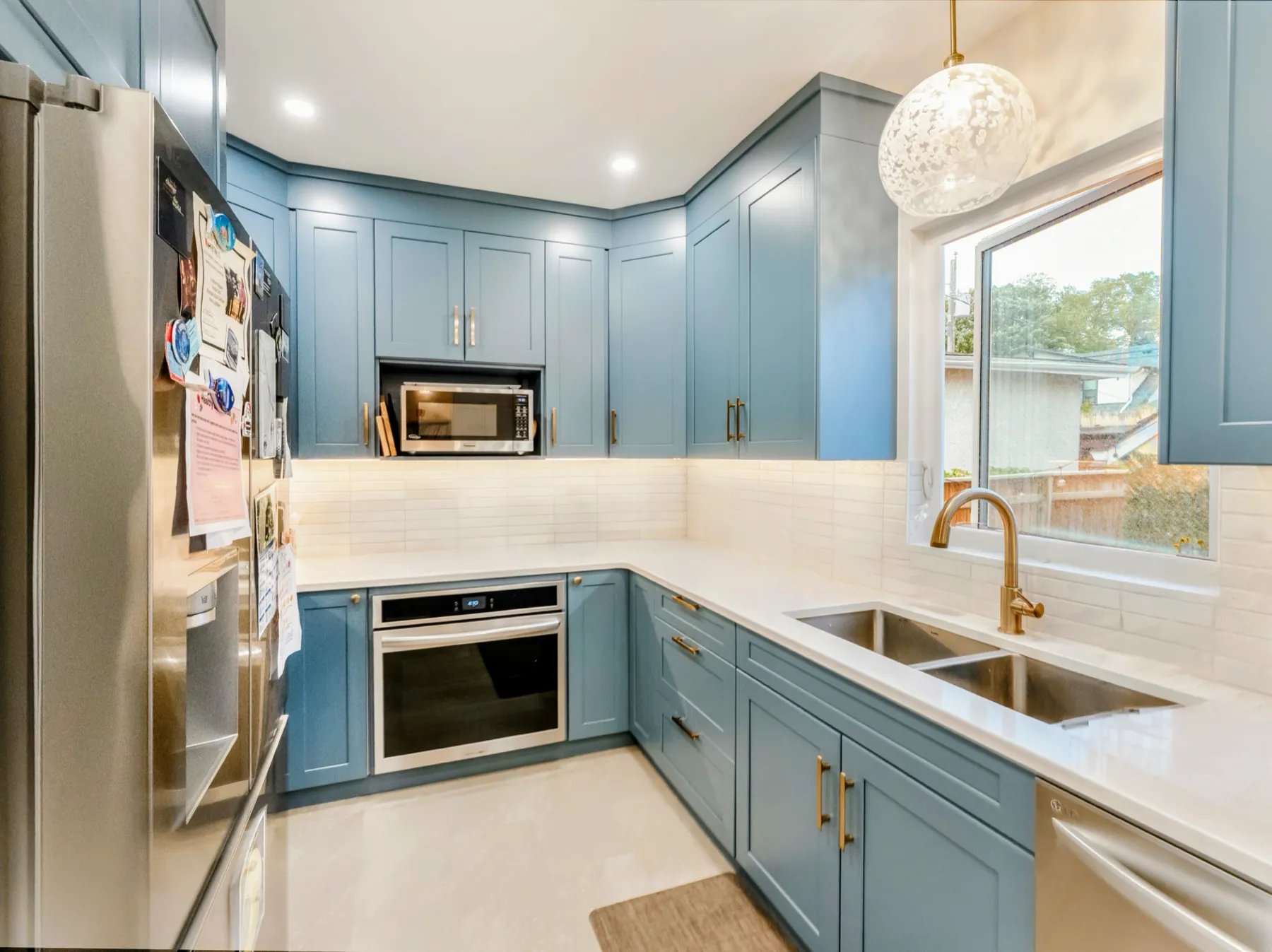 Sink and brass tap under the window, blue cabinetry either side
