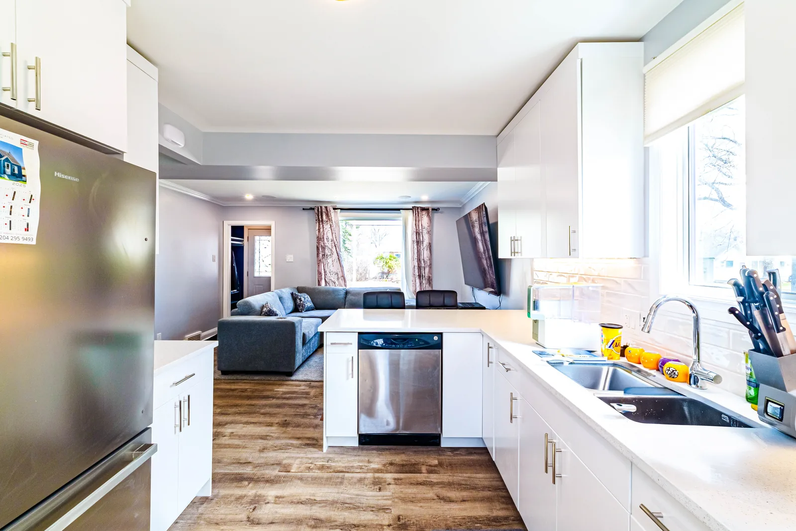 White gloss kitchen with a long island, stainless appliances and grey plank flooring