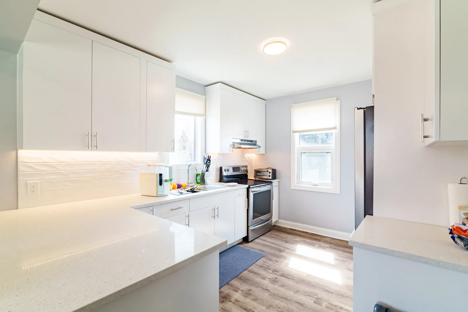 The gloss-white kitchen from the far end, the island and counter run under a window