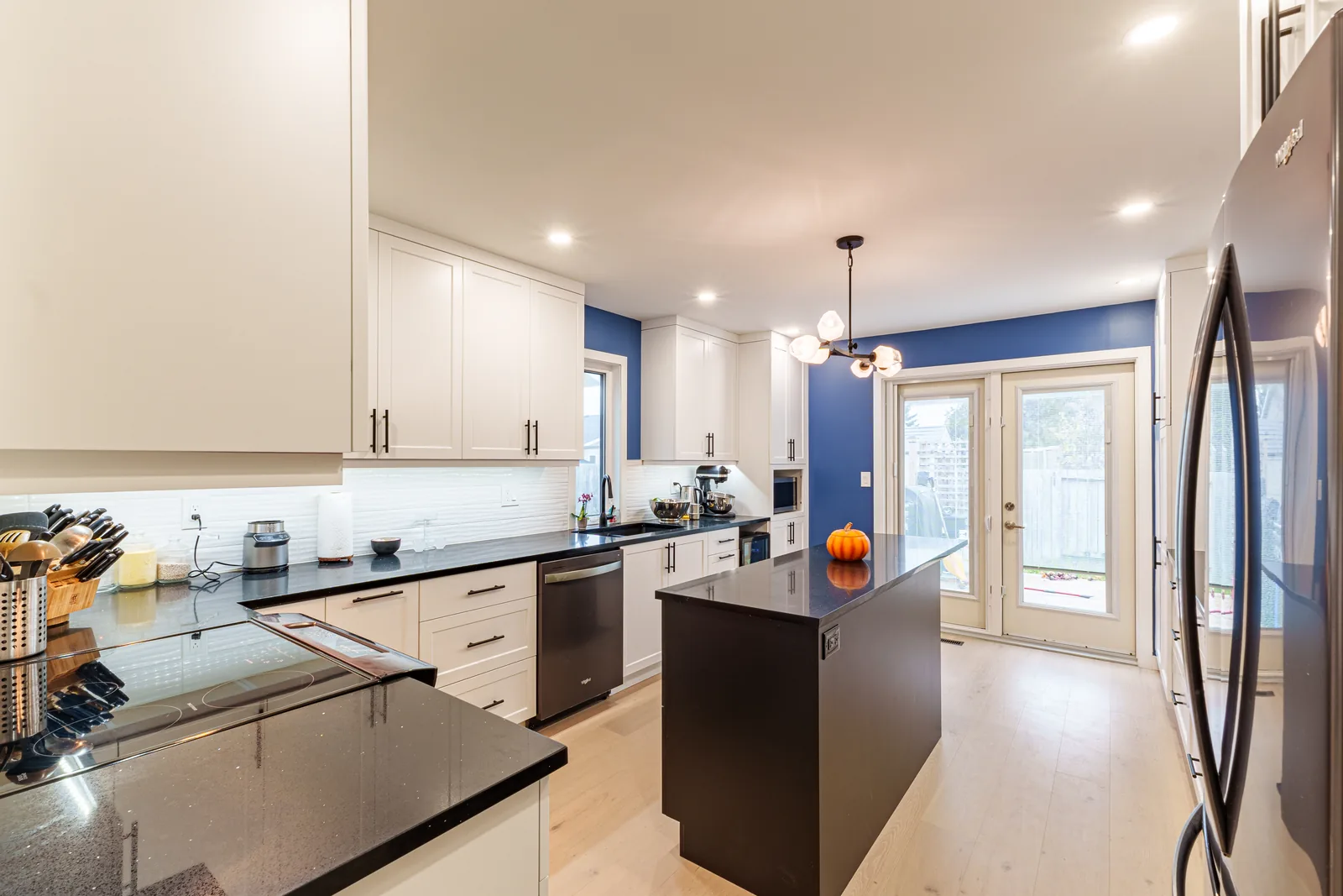 White and blue kitchen — white shaker cabinetry to the ceiling against navy walls, a navy island under a black quartz top, and stainless appliances