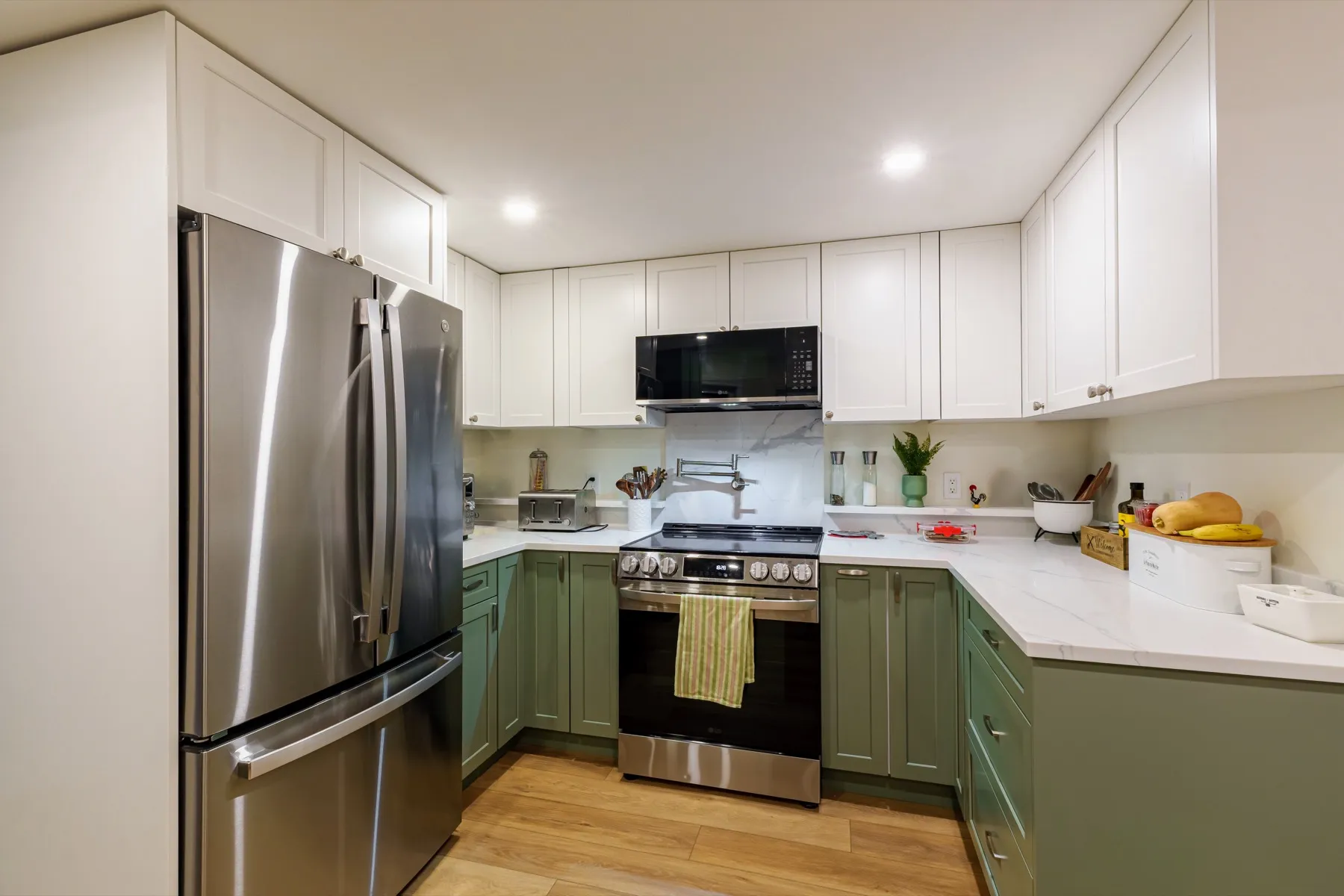 The L-shaped kitchen: olive bases, white uppers to the ceiling, the range and fridge along the run