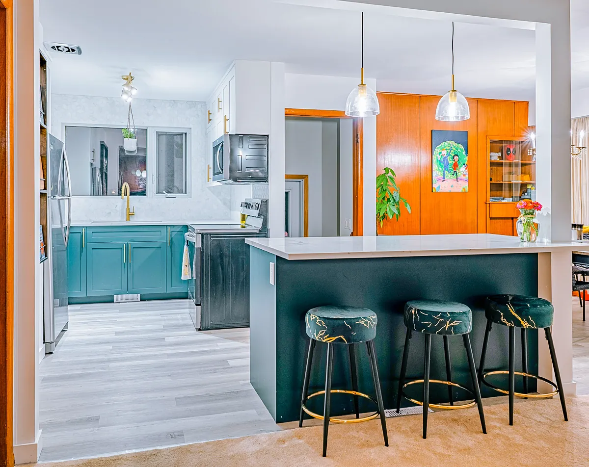 Teal kitchen with a white quartz island, brass hardware and green velvet stools