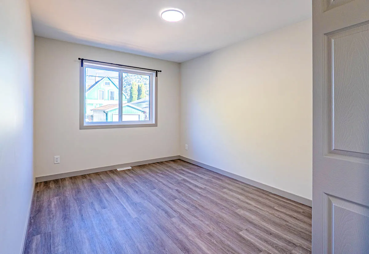 A bedroom with a window onto the street, vinyl plank floor