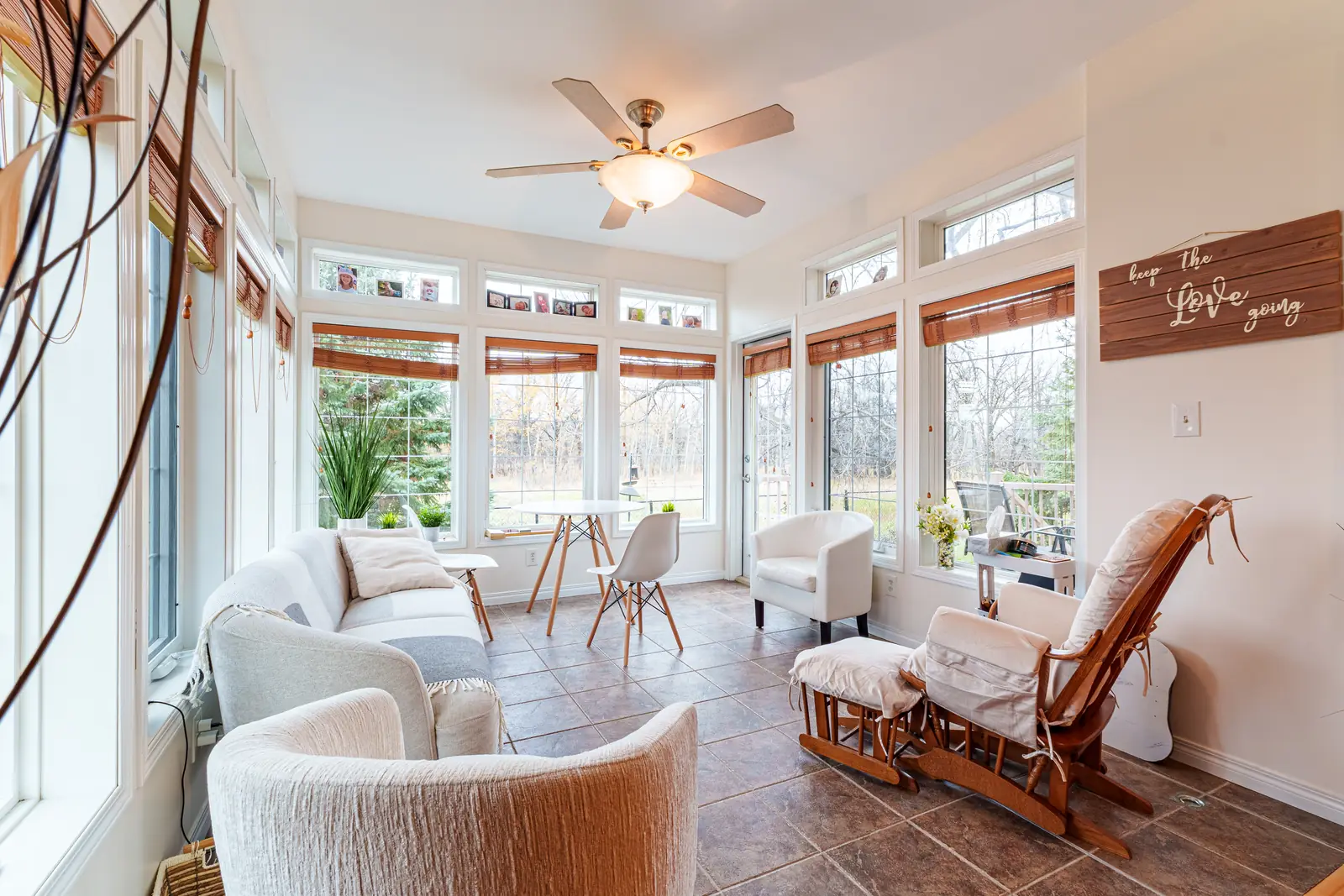 Four-season room with windows on three sides, transoms above and seating under a ceiling fan