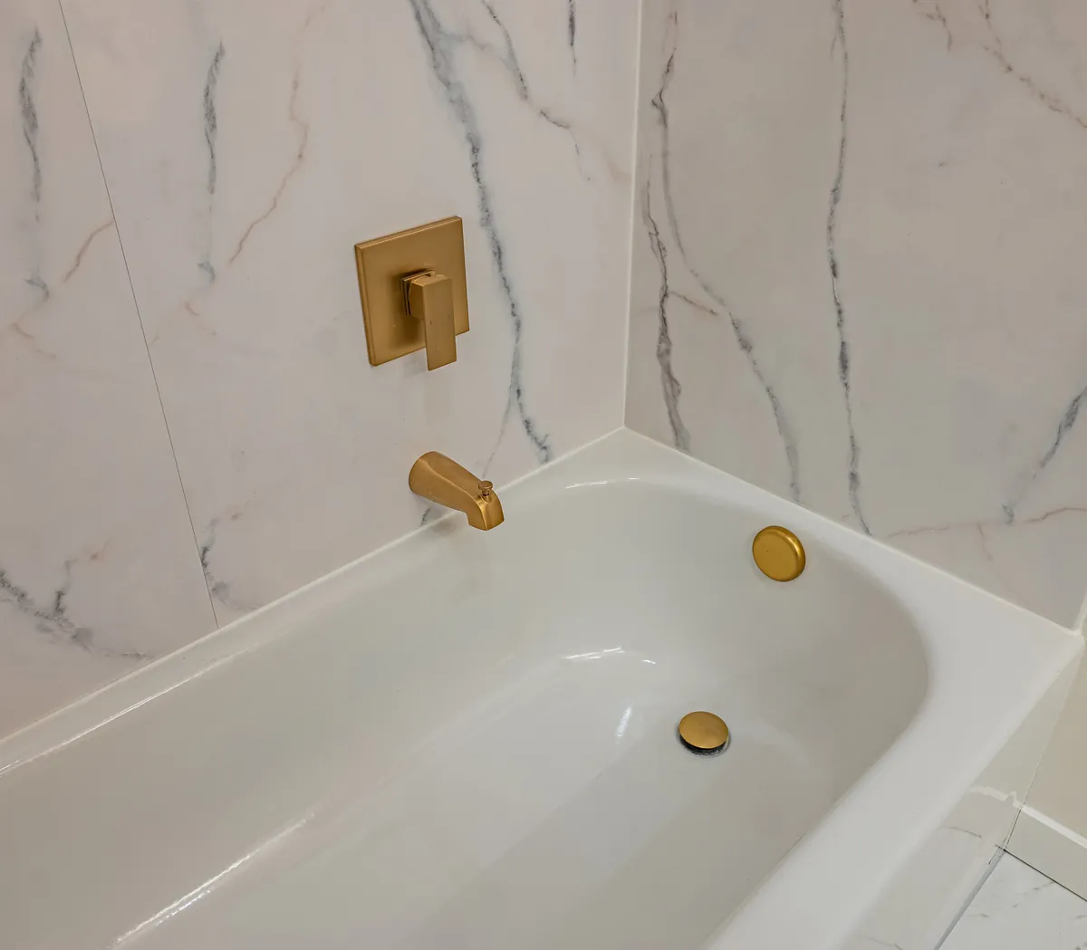 The tub's gold spout and controls against the veined tile