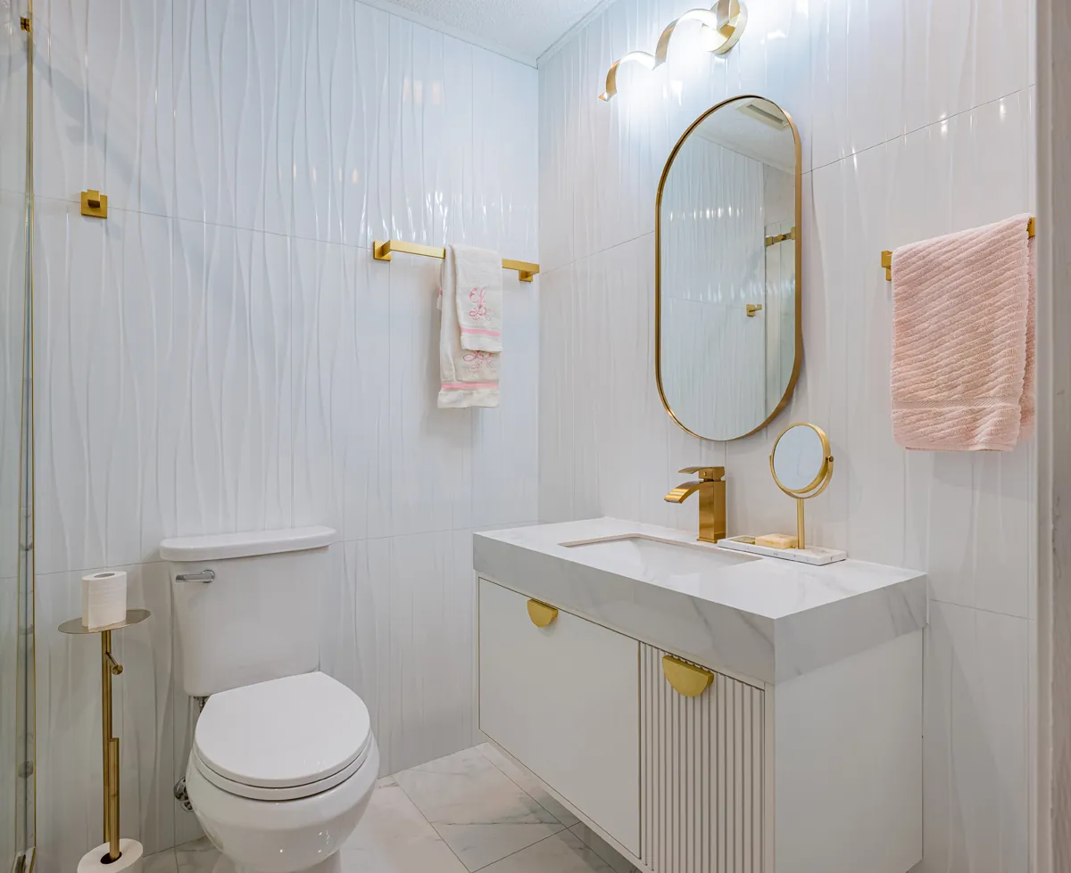 Third bathroom, a fluted floating vanity under an oval gold mirror, ribbed white tile
